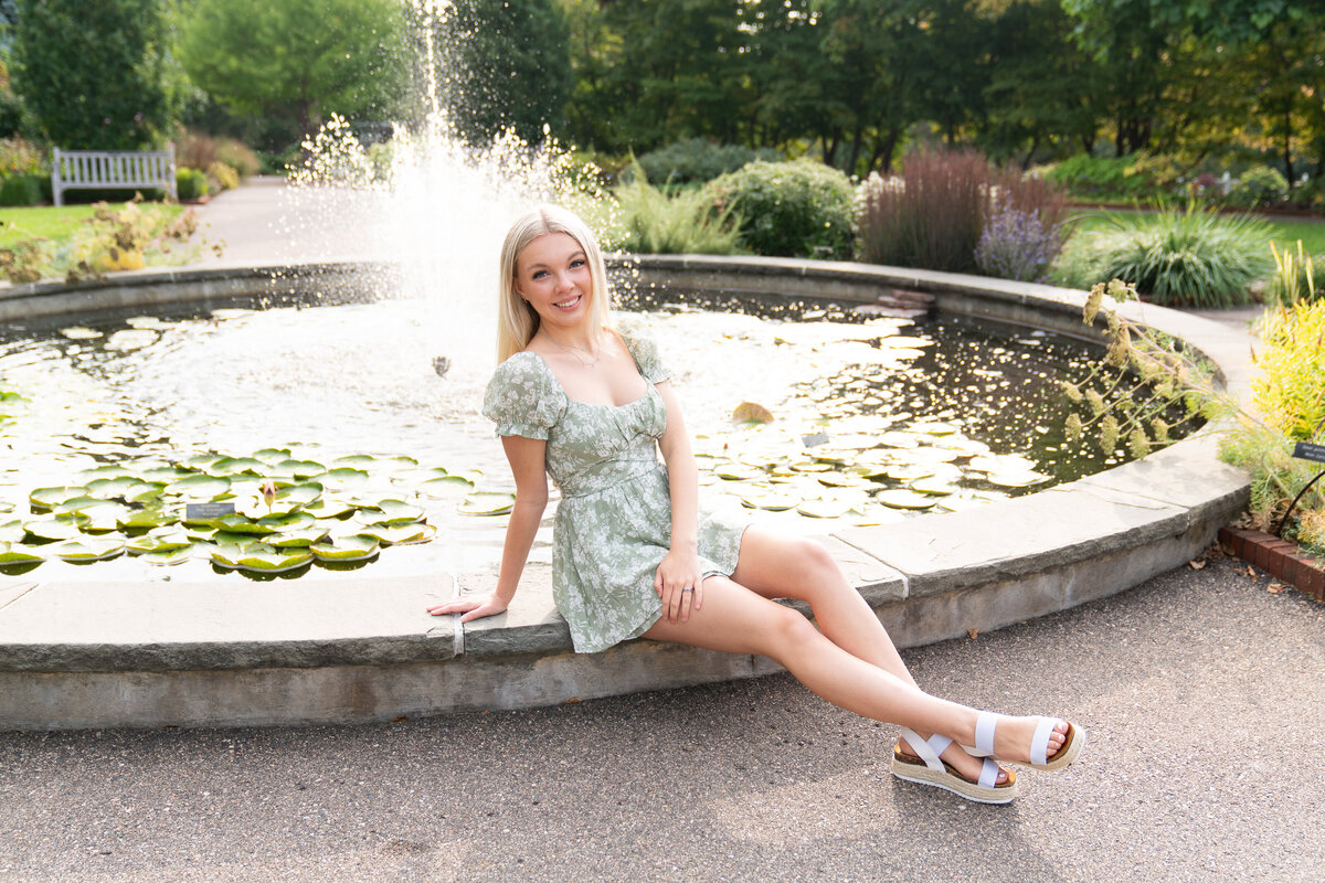 High school senior girl wearing a dress sitting on a fountain