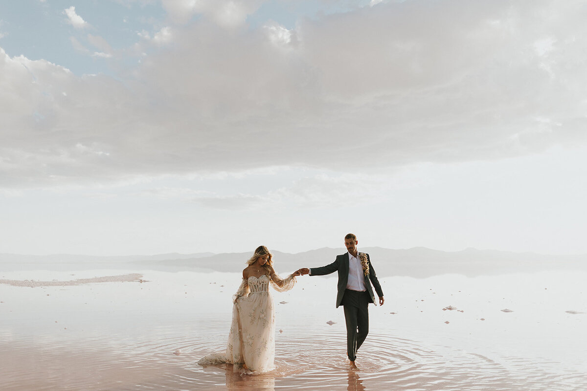 A couple eloping in Salt Lake City, Utah, walking towards the camera near a pink-hued lake, exuding romance and elegance.