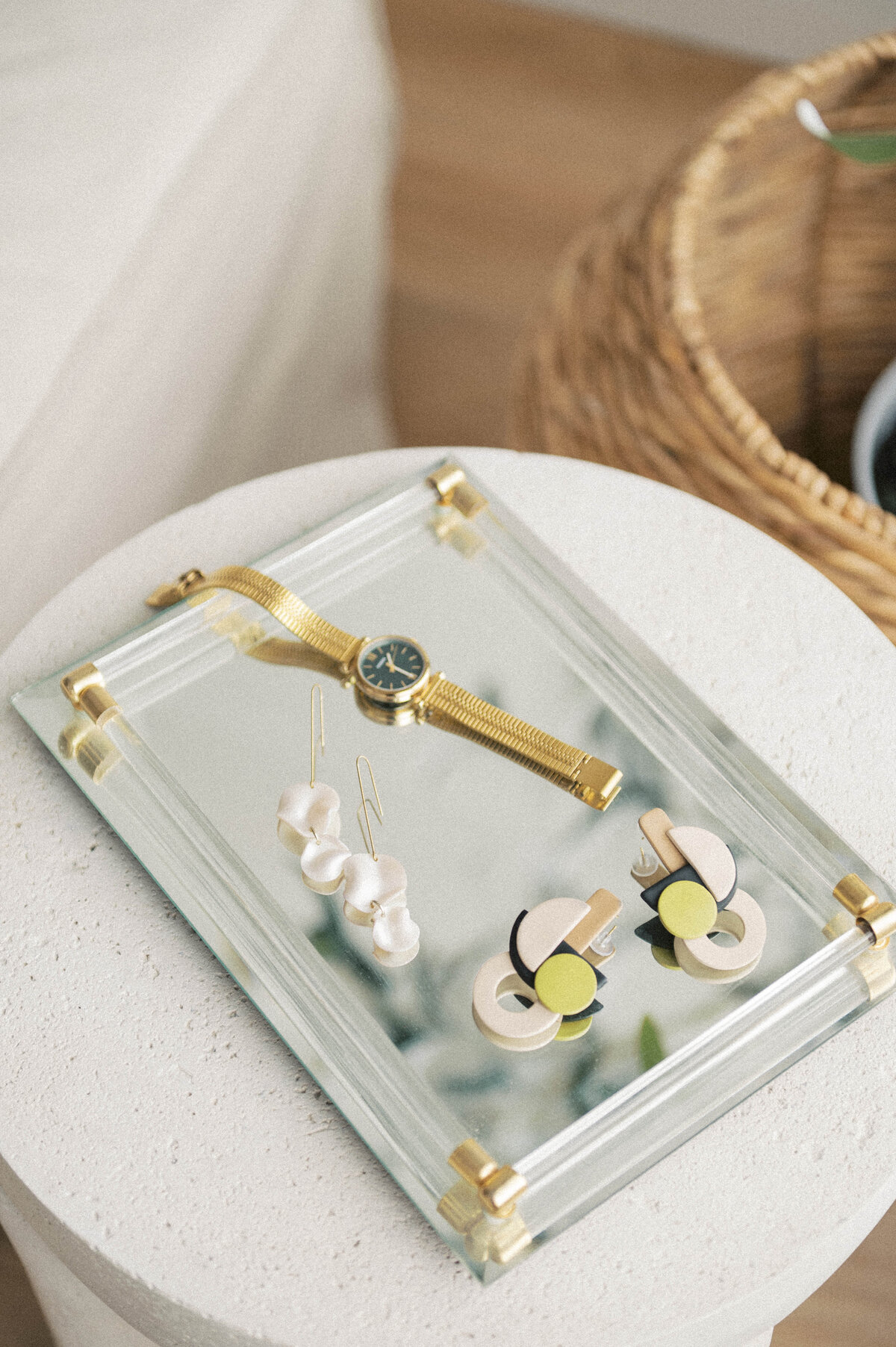 Gold watch and colourful earrings sitting on a mirrored tray