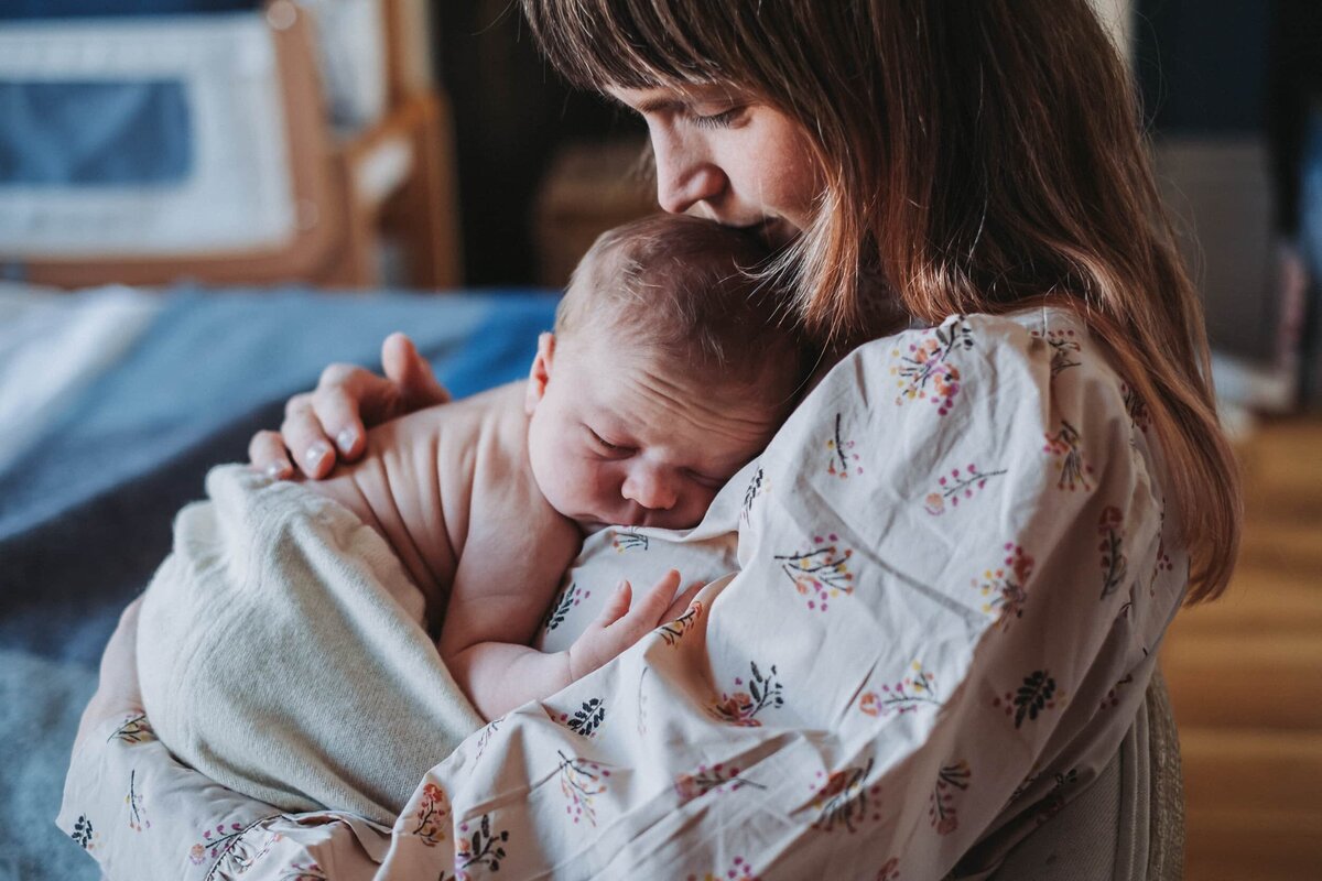 Naked baby cuddles with mum who kisses his head while he sleeps