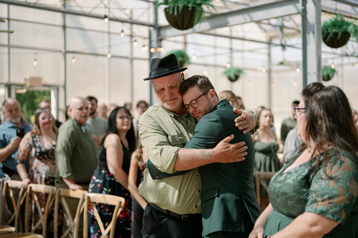Emotional embrace between the groom and his father during the Ivy House greenhouse ceremony.