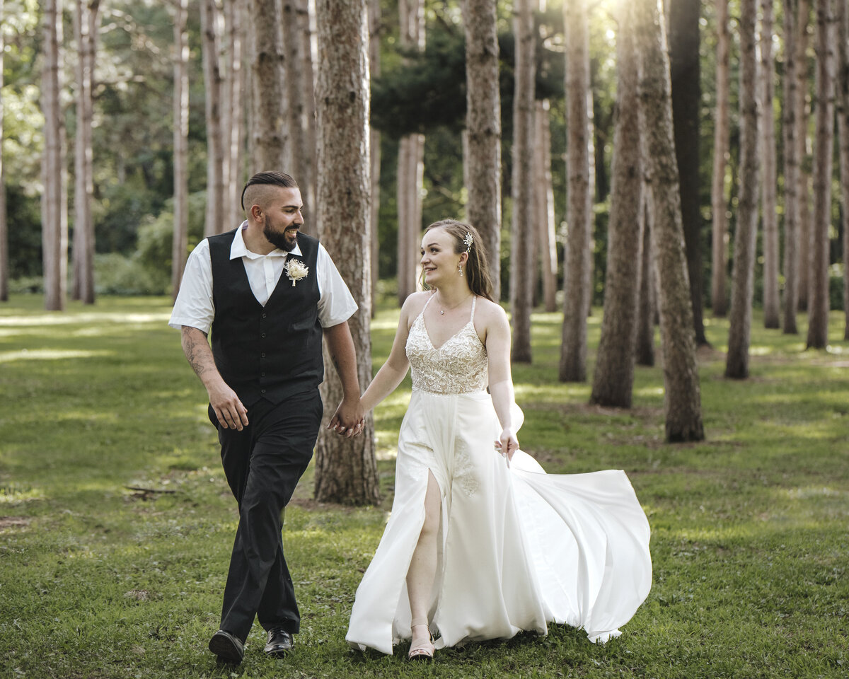 A joyful bridal couple walking hand in hand among tall trees, basking in the serene glow of their wedding day taken by jen Jarmuzek photography a Minneapolis wedding photographer