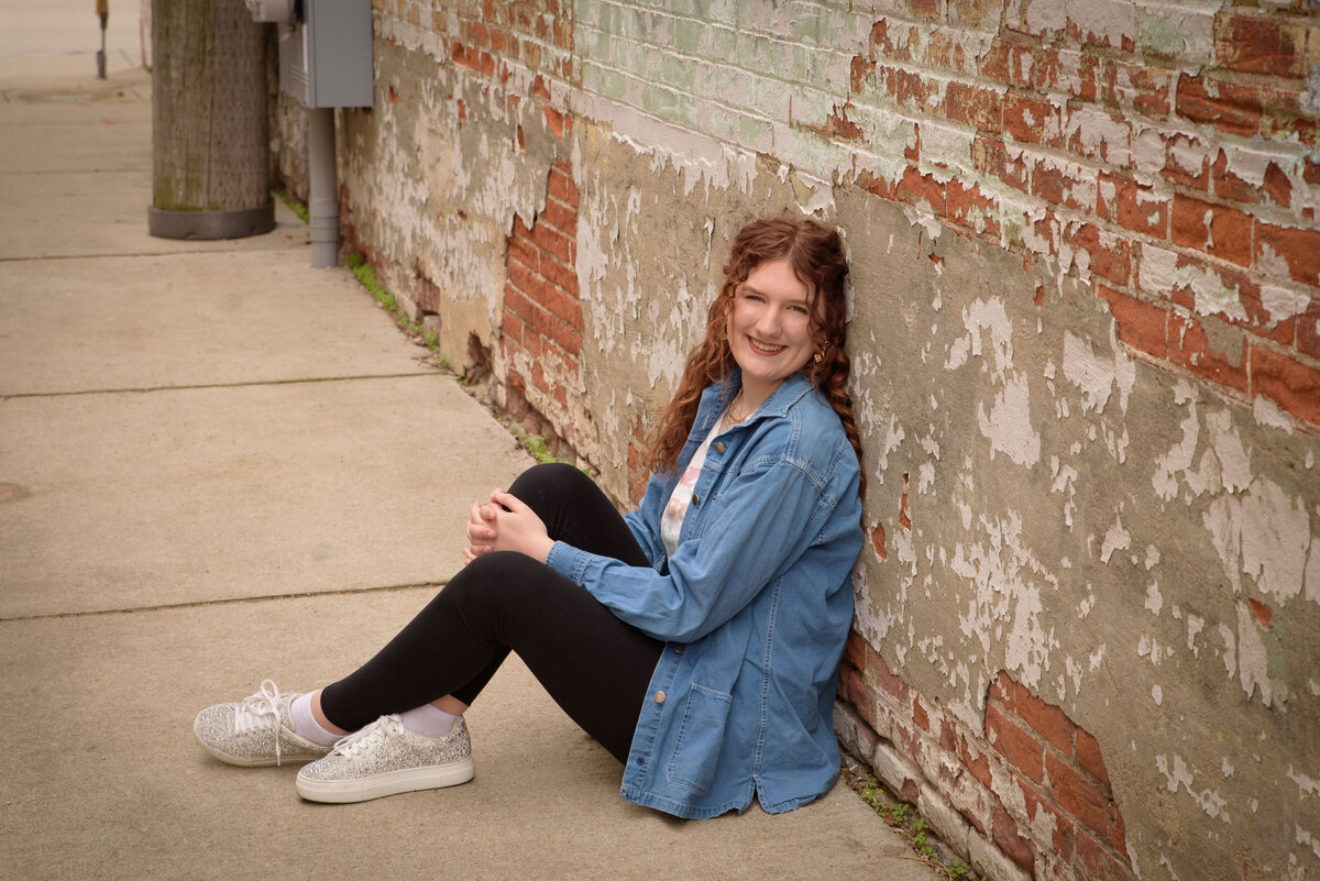 Green Bay East High School senior girl wearing a graphic t-shirt and leggings sitting in a brick alley way in an urban setting in downtown Green Bay, Wisconsin