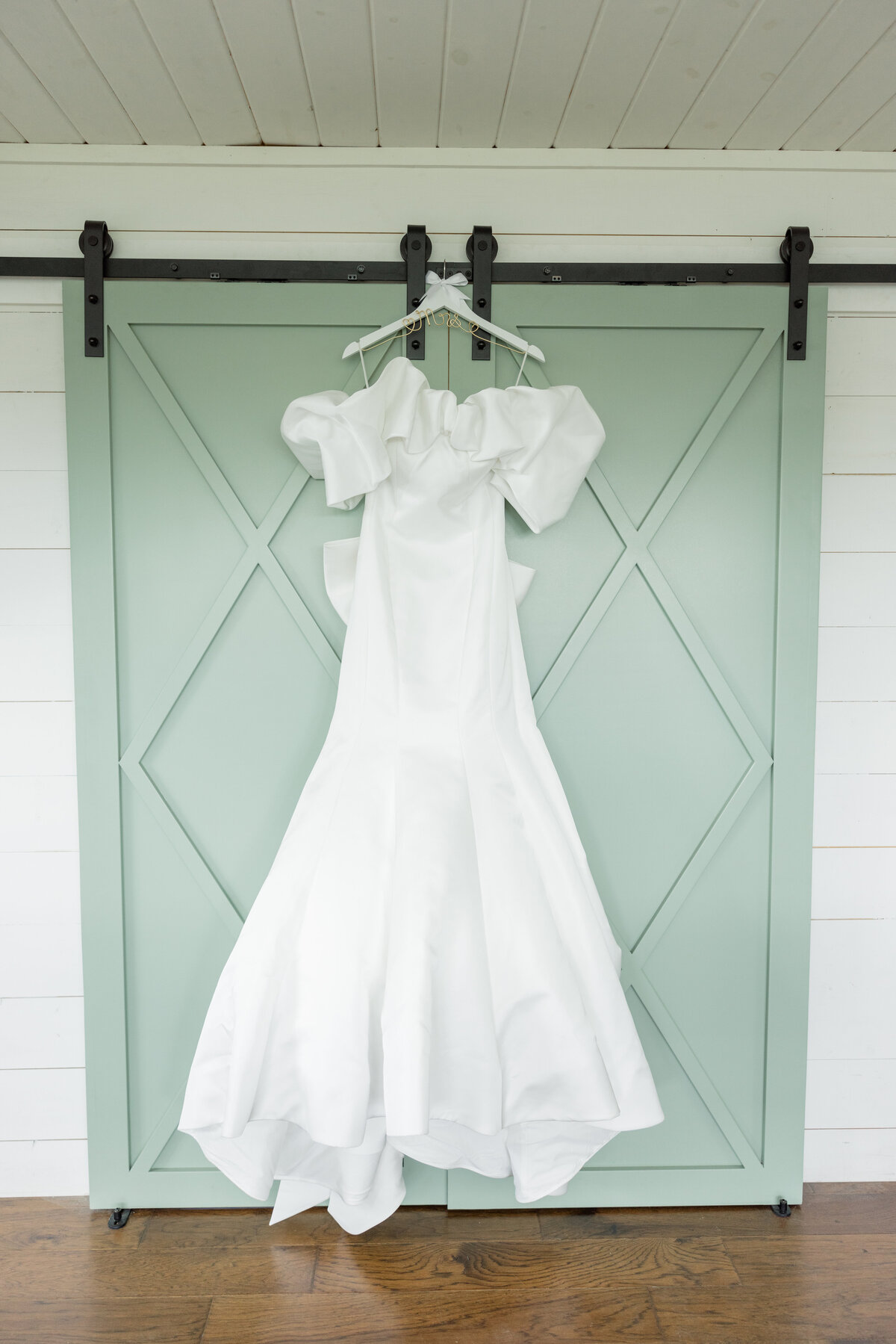 Wedding gown hung in bridal cottage in front of sage green barn doors. 