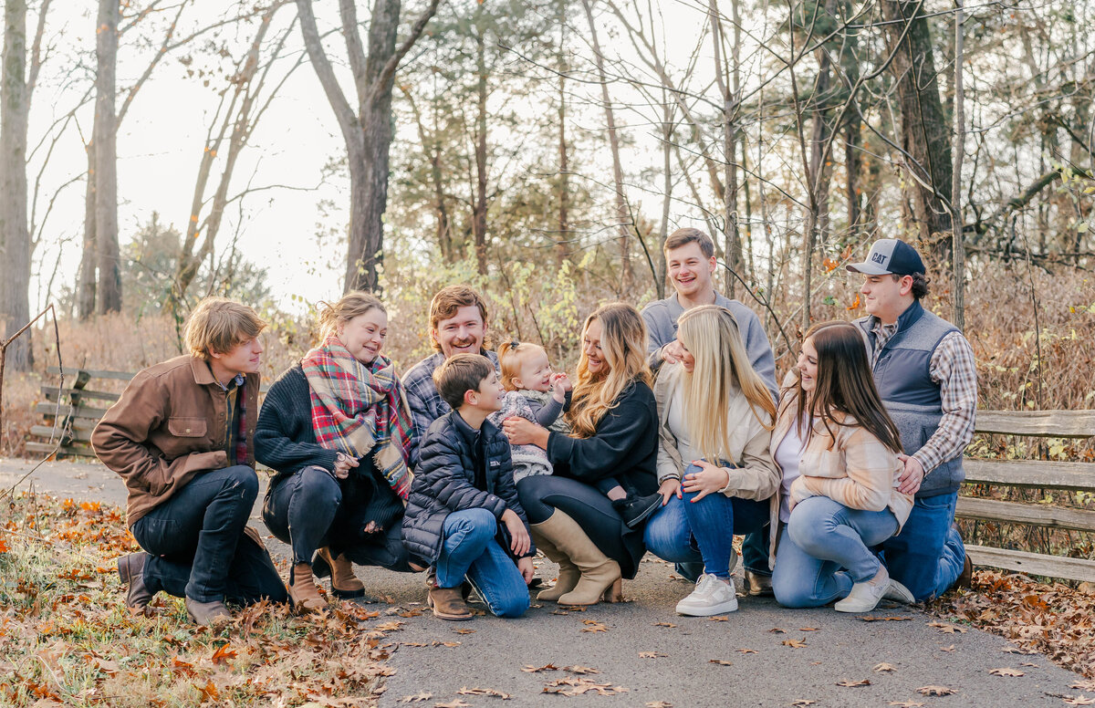 outdoor extended family photo shoot with everyone looking at the baby and laughing at her silliness