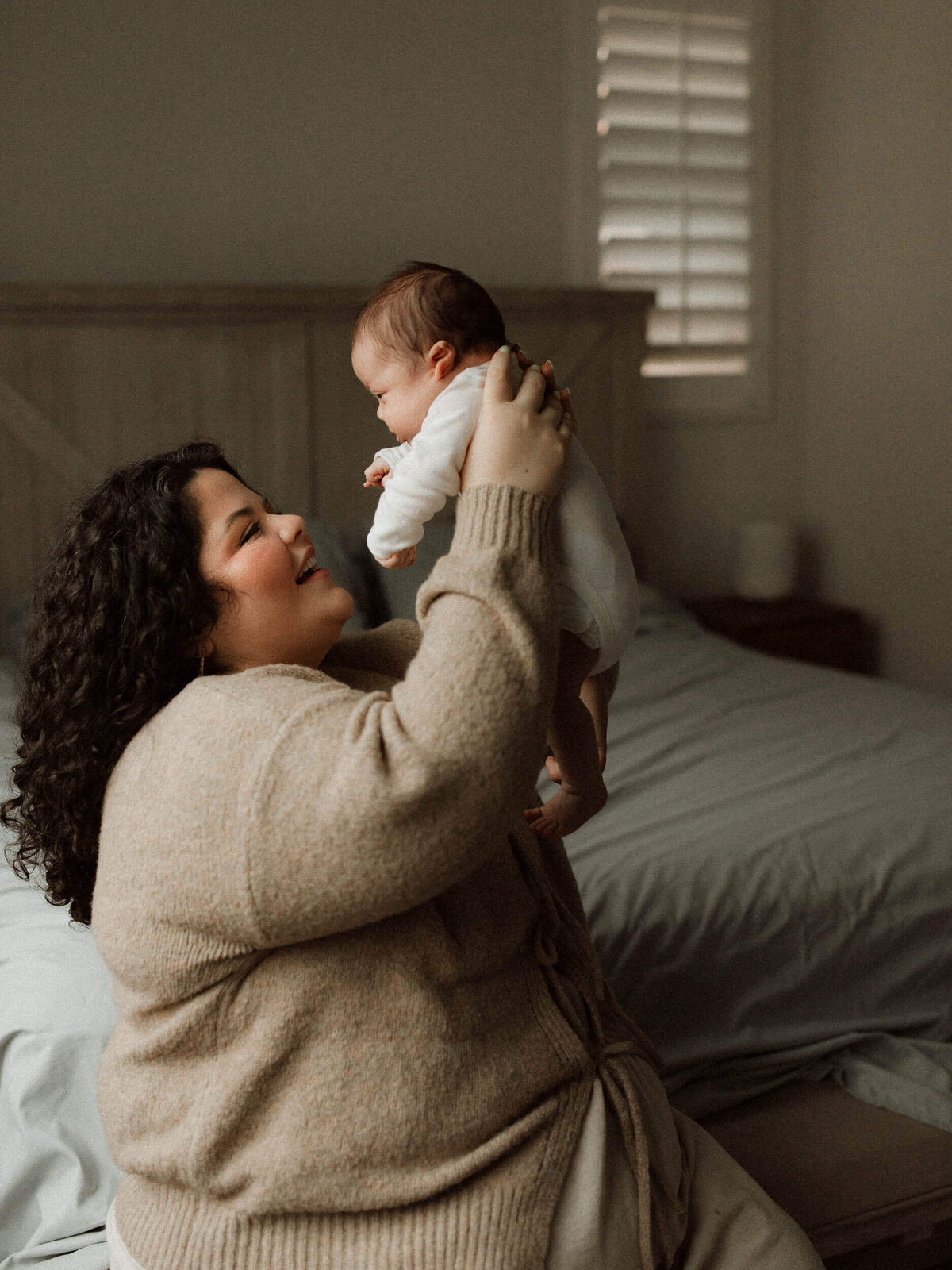 Mother holding her newborn up in the air in an intimate lifestyle portrait.