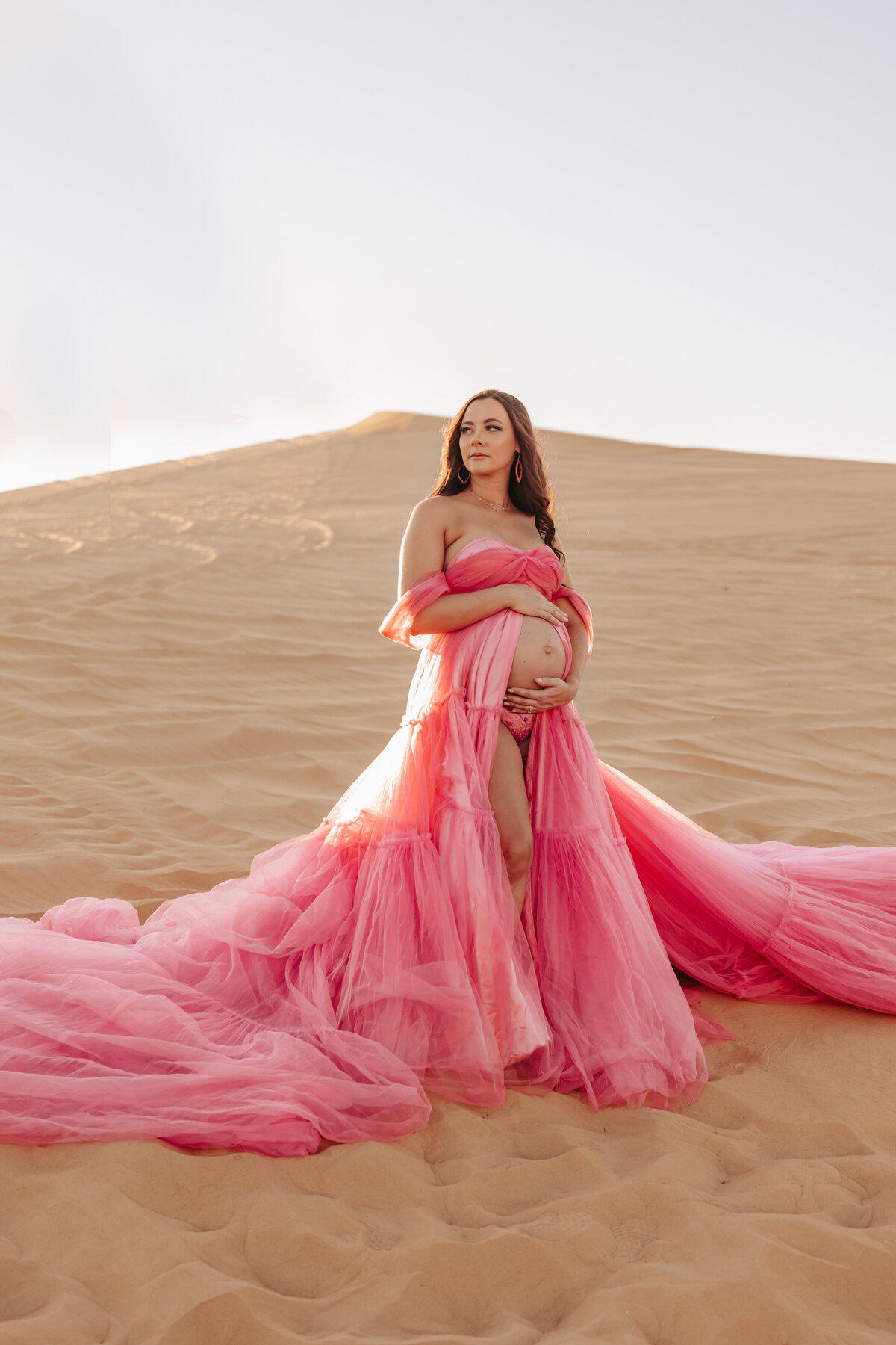 mother wearing bright pink tulle maternity gown holding her baby bump
