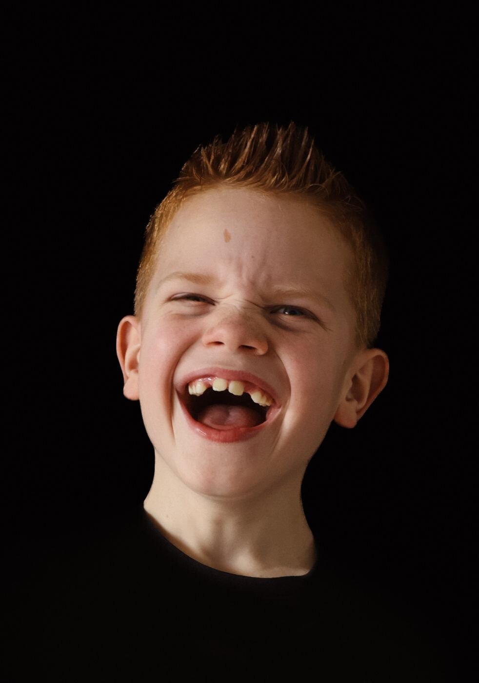 Een zwart-wit portretfoto van een lachende baby, gefotografeerd tegen een donkere achtergrond.