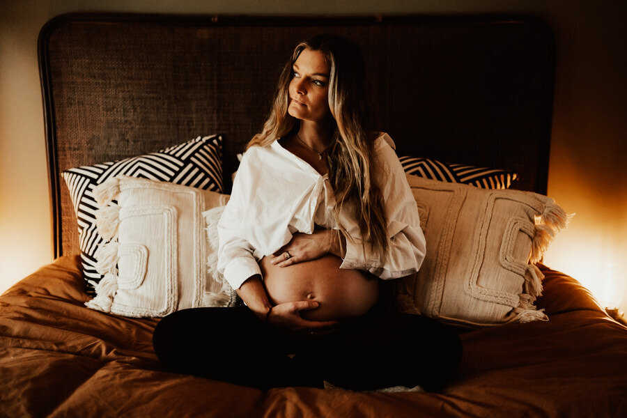 gravid sitter på säng i bohemiskt hem och håller om magen
