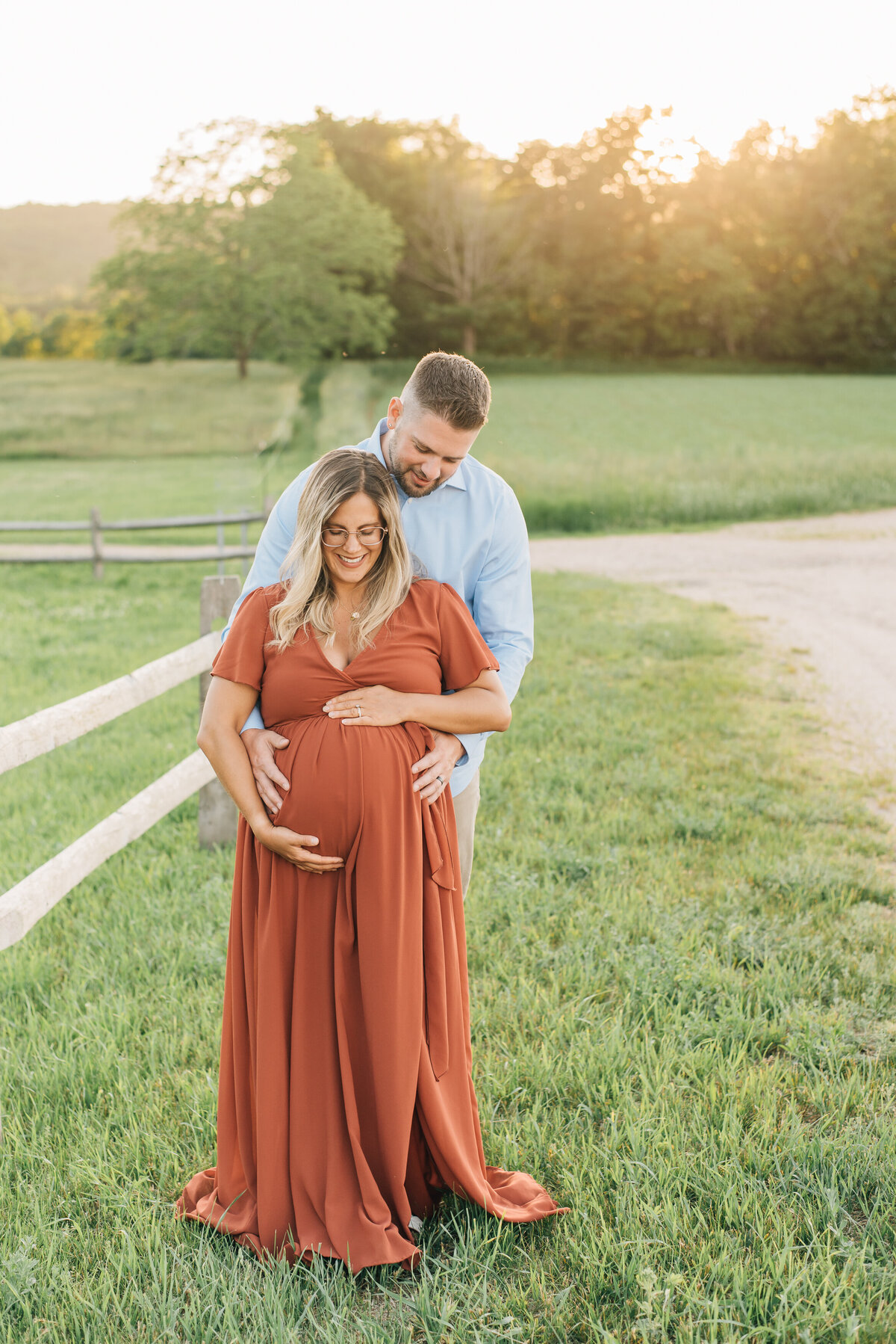 Expecting mom and dad, smiling down at baby in field at sunset
