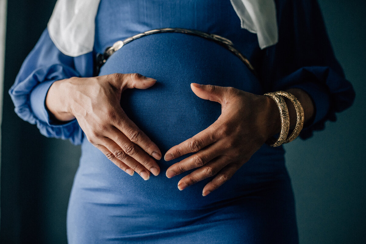 Maternity shot of soon to be mom wearing a blue dress and holding her belly.
