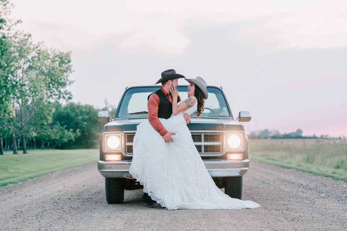 Bride and groom standing on a gravel  road by Dalmeny SK. An old truck is behind them.