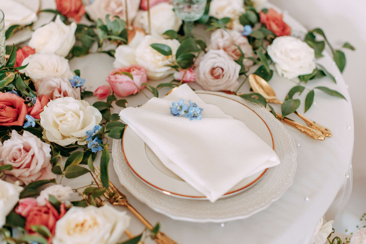 wedding table setting with napkin and gold rimmed plate with florals