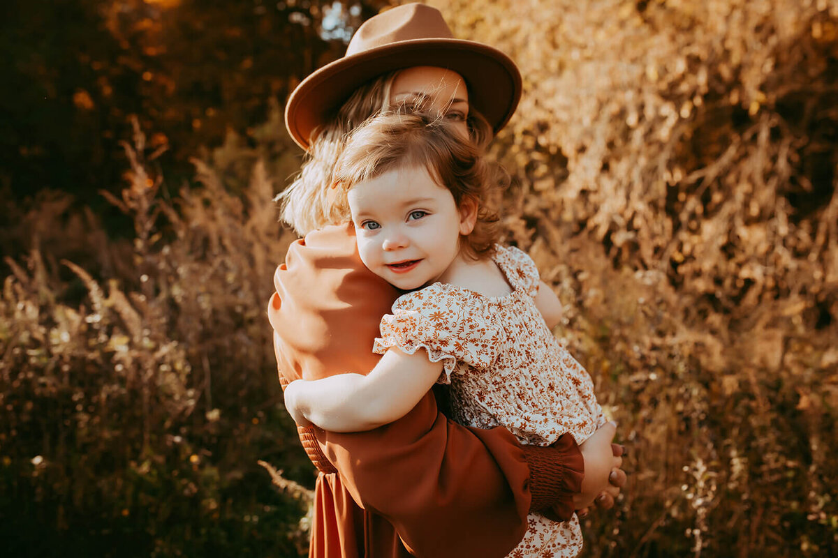 a mother wearing a hat holding her daughter in a gorgeous field in rochester, ny