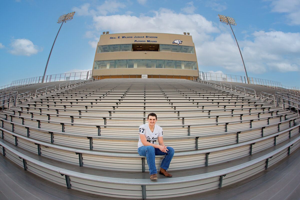 A high school senior guy poses on his high school football stadium for senior pictures.