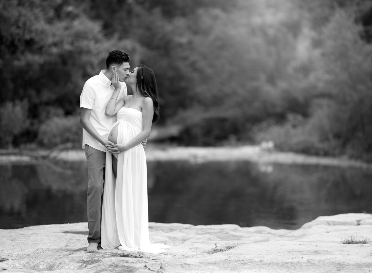 pregnant couple kissing by a creek