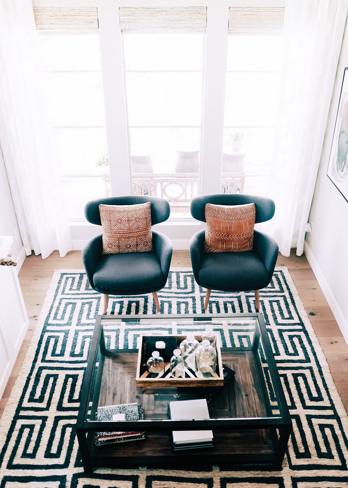 Two blue armchairs with red boho cushions with a monochrome pattered rug.