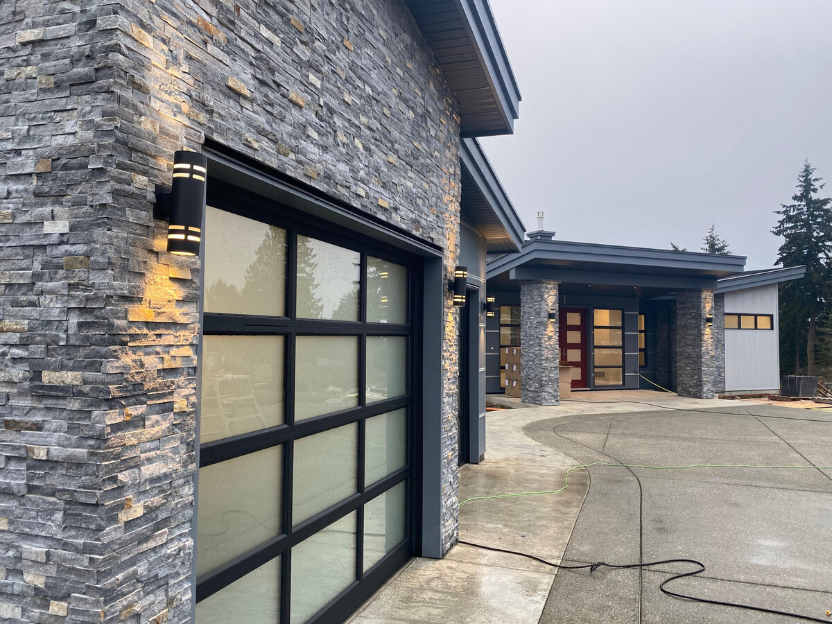 Contemporary home design exterior entry with stone wrapped pillars and glass garage doors.