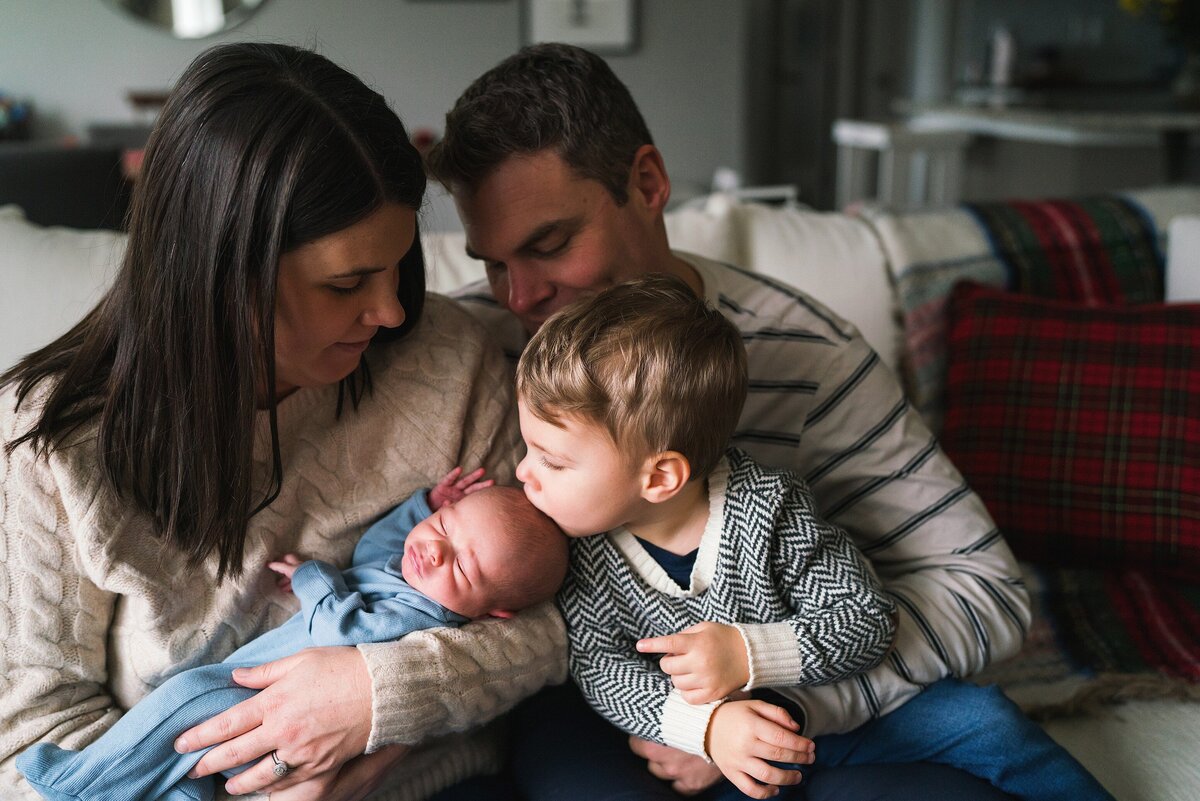 Big brother giving baby brother kiss  as parents watch lovingly