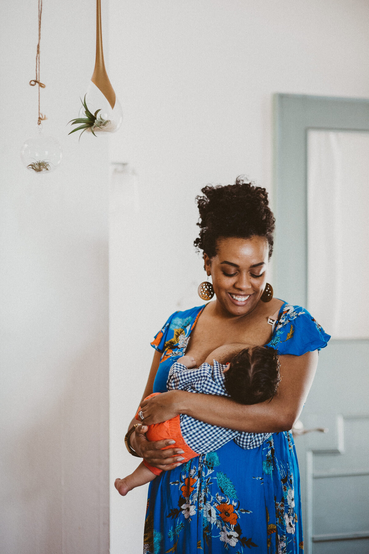 black mother breastfeeds her baby while standing in her home