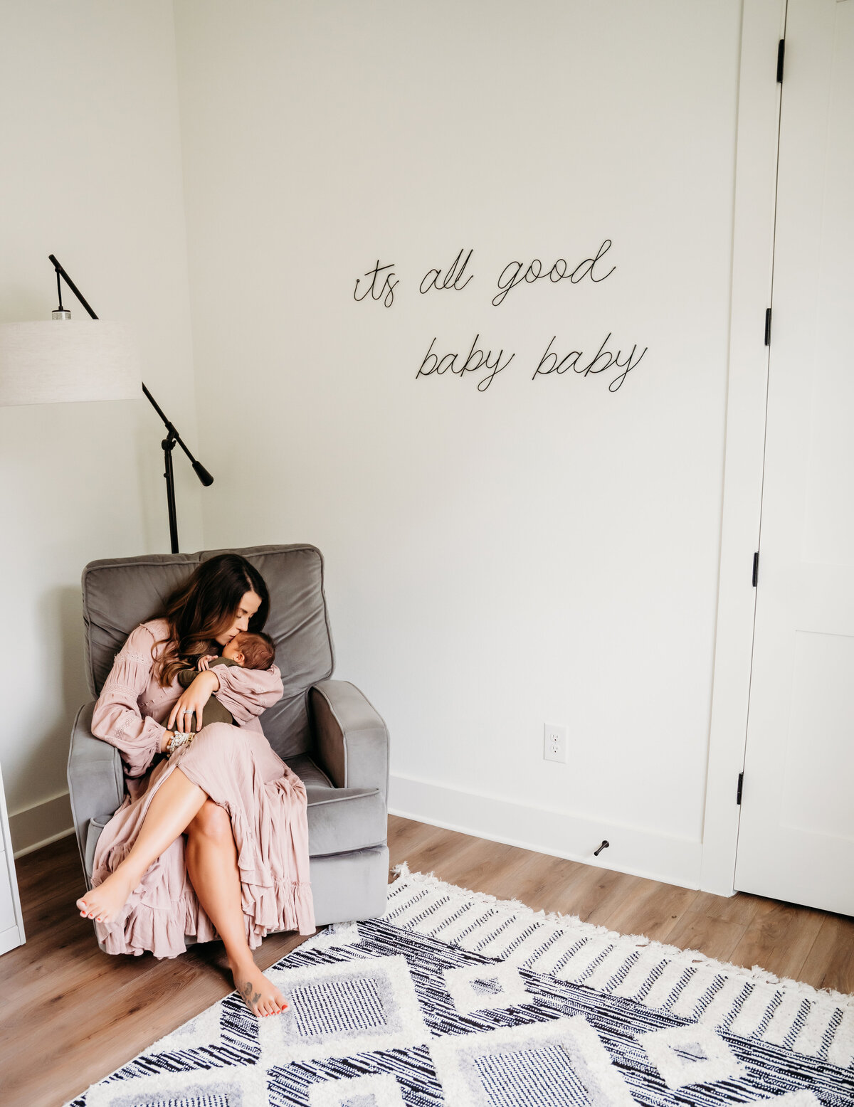 Newborn Photographer, a mother sits in a corner chair in her room doting on baby