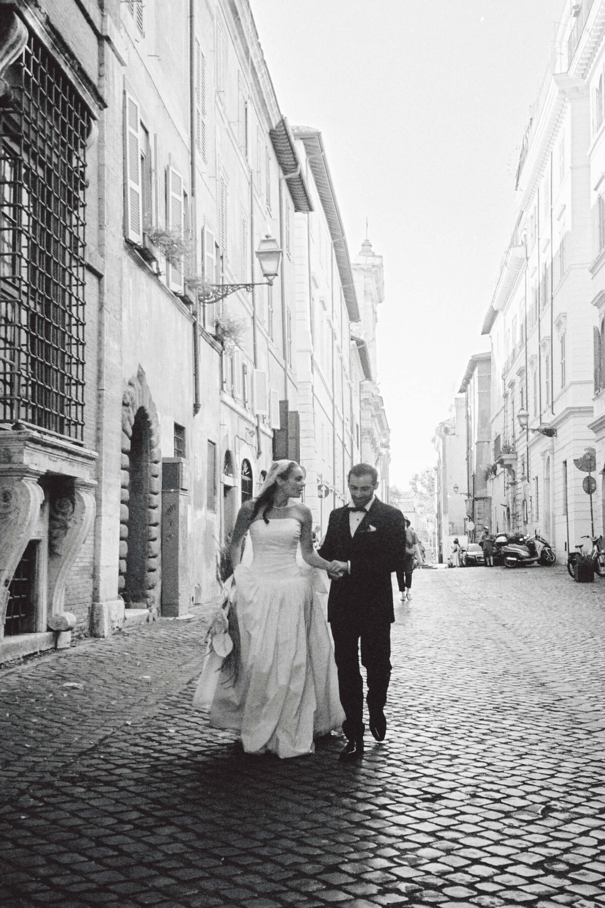 Black and white image of newlyweds walking through historic Roman alley

