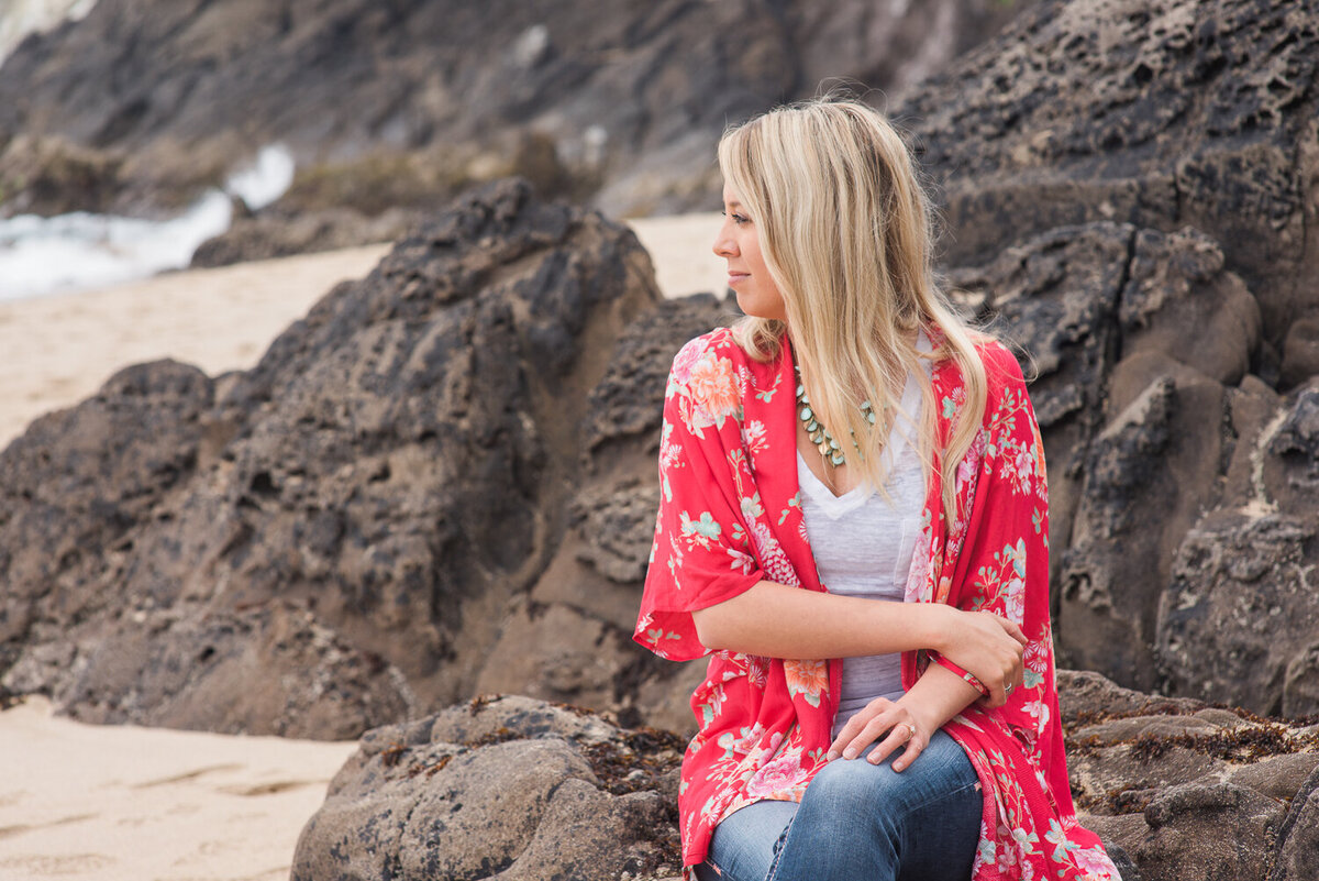 Natural portrait of a young woman with long, blonde hair and red shirt, sitting on a rock on the beach