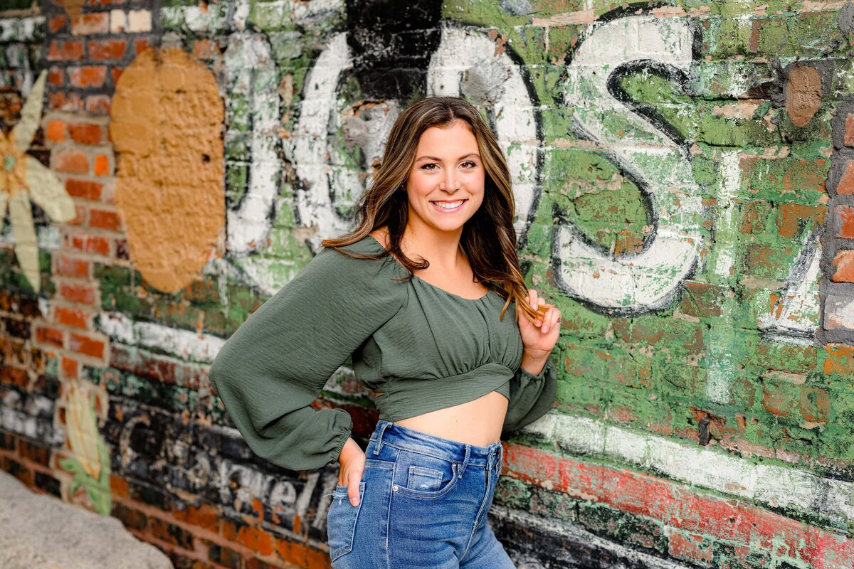 cuthbertson high school graduate leans against a wall wearing a green crop top with jeans