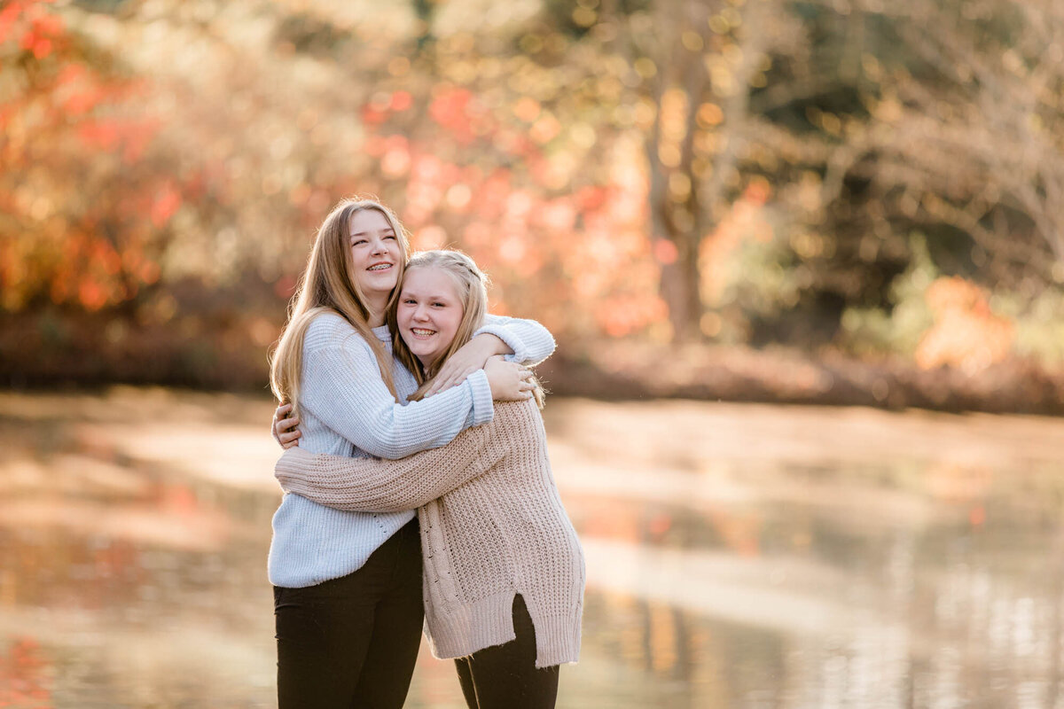 Two sisters laughing and hugging each other for a family portrait.