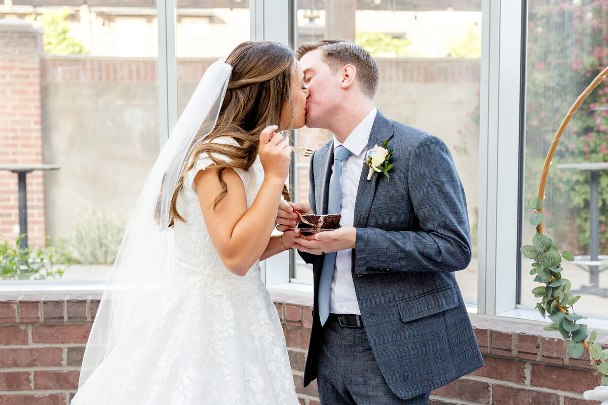 A bride and groom share a sweet moment as they feed each other wedding cake, ending in a playful kiss.
