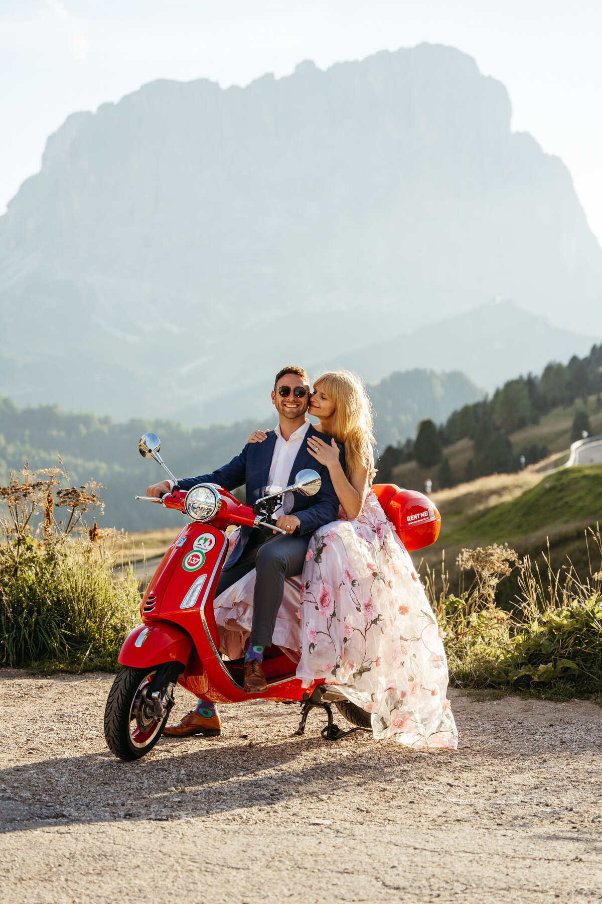 Bride and groom riding red Vespa through Dolomites mountain road