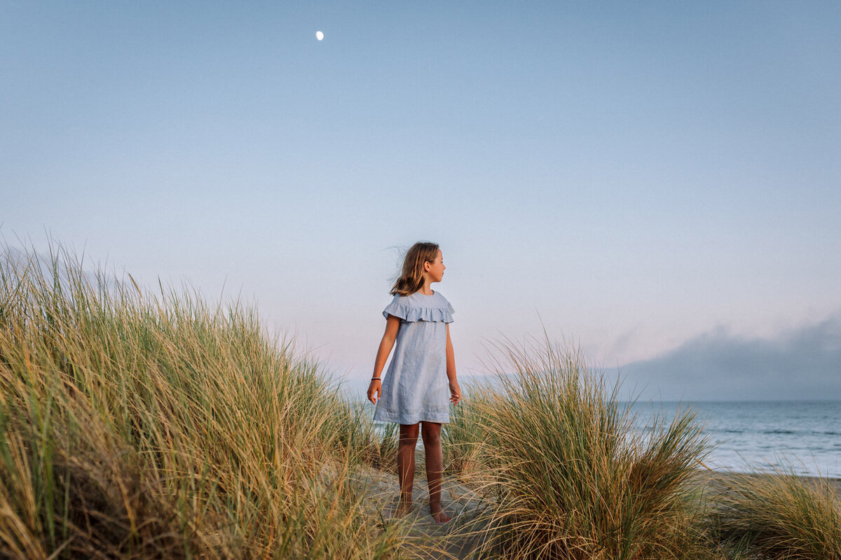 7-year-old-girl standing by tall sea grass looking towards pacific ocean in Marin