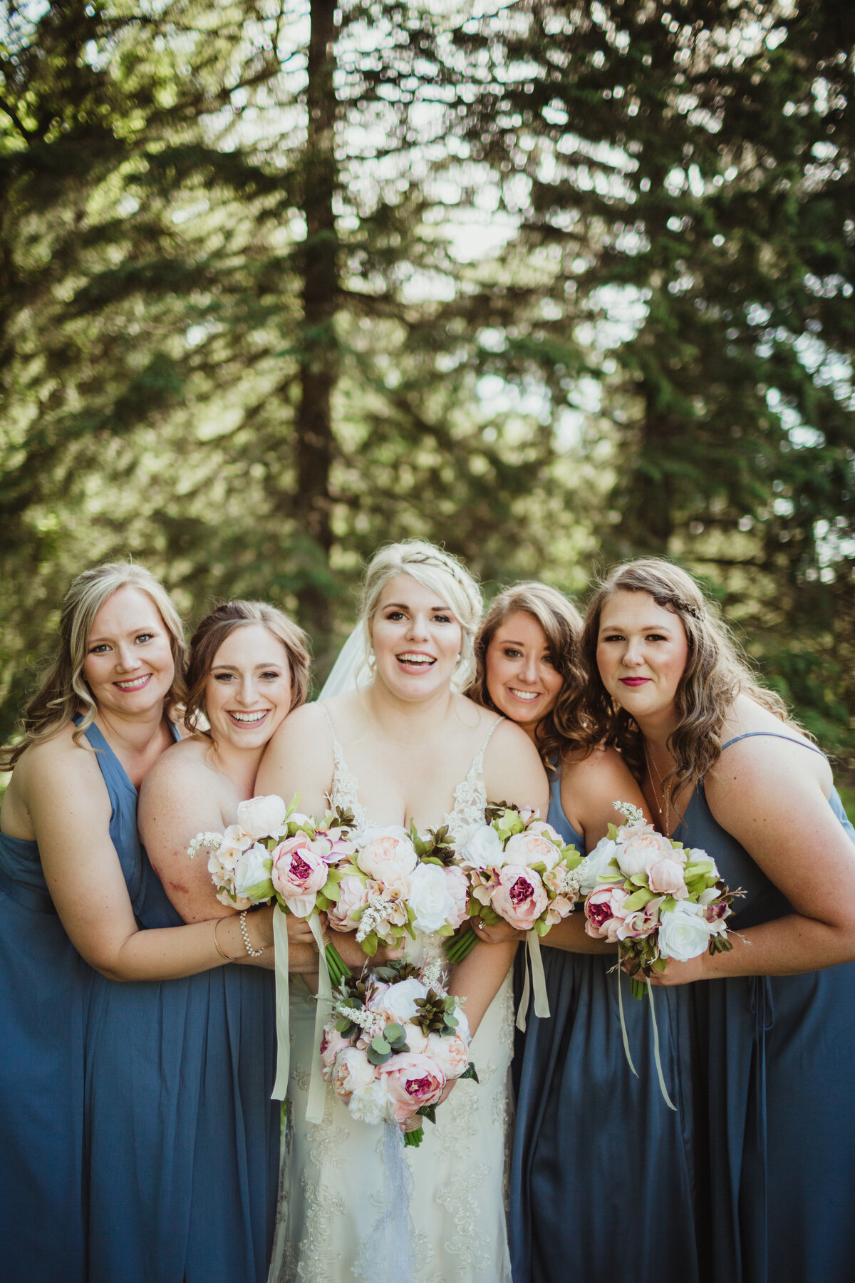 Bride with bridesmaids in blue dresses with trees in background