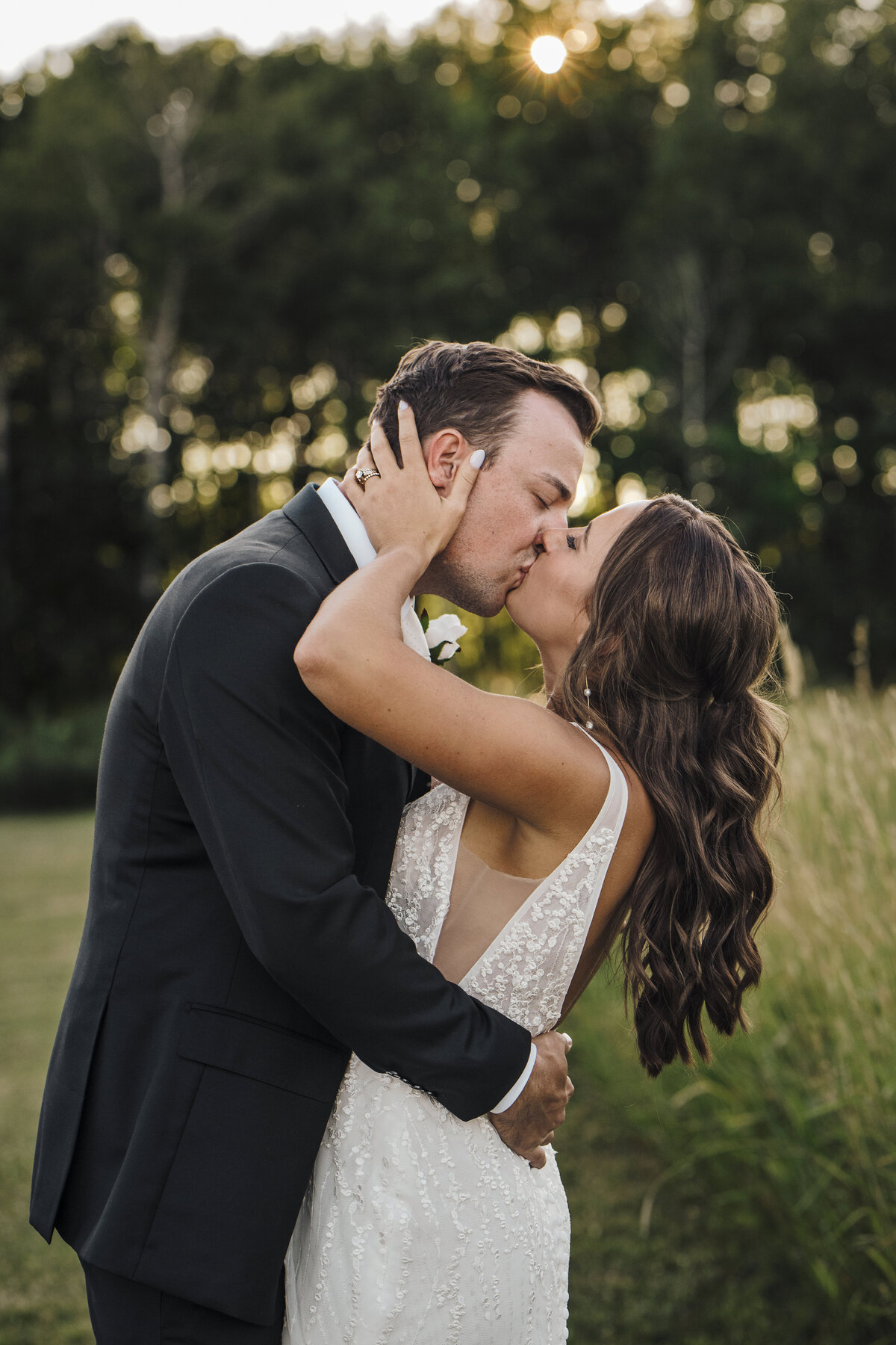 A tender moment captured as a couple in wedding attire share a passionate kiss, surrounded by the tranquility of nature with the soft glow of sunset in the background taken by jen Jarmuzek photography a Minneapolis wedding photographer