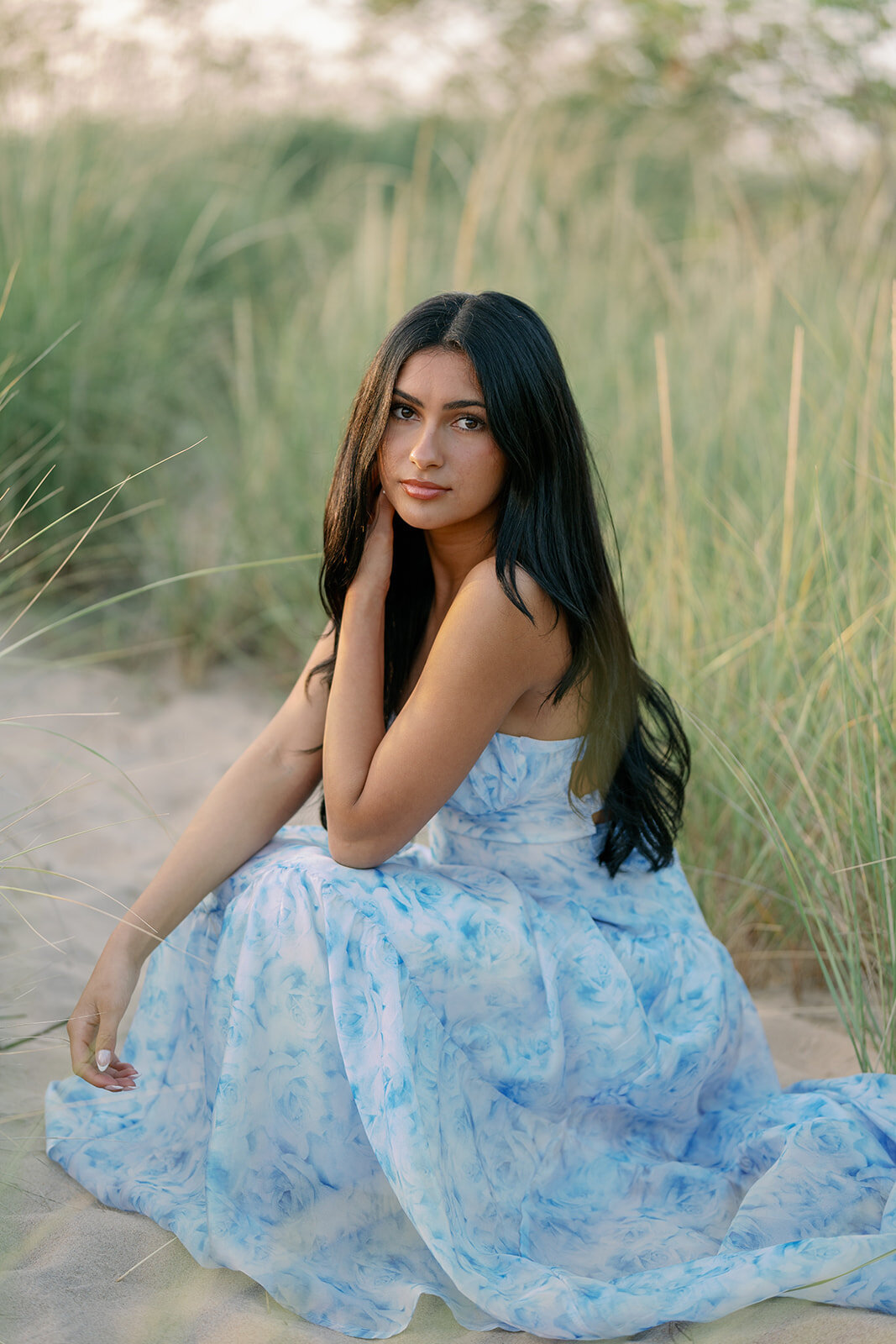 Teen girl kneeling in dune grass during her South Haven senior photo session at North Beach.
