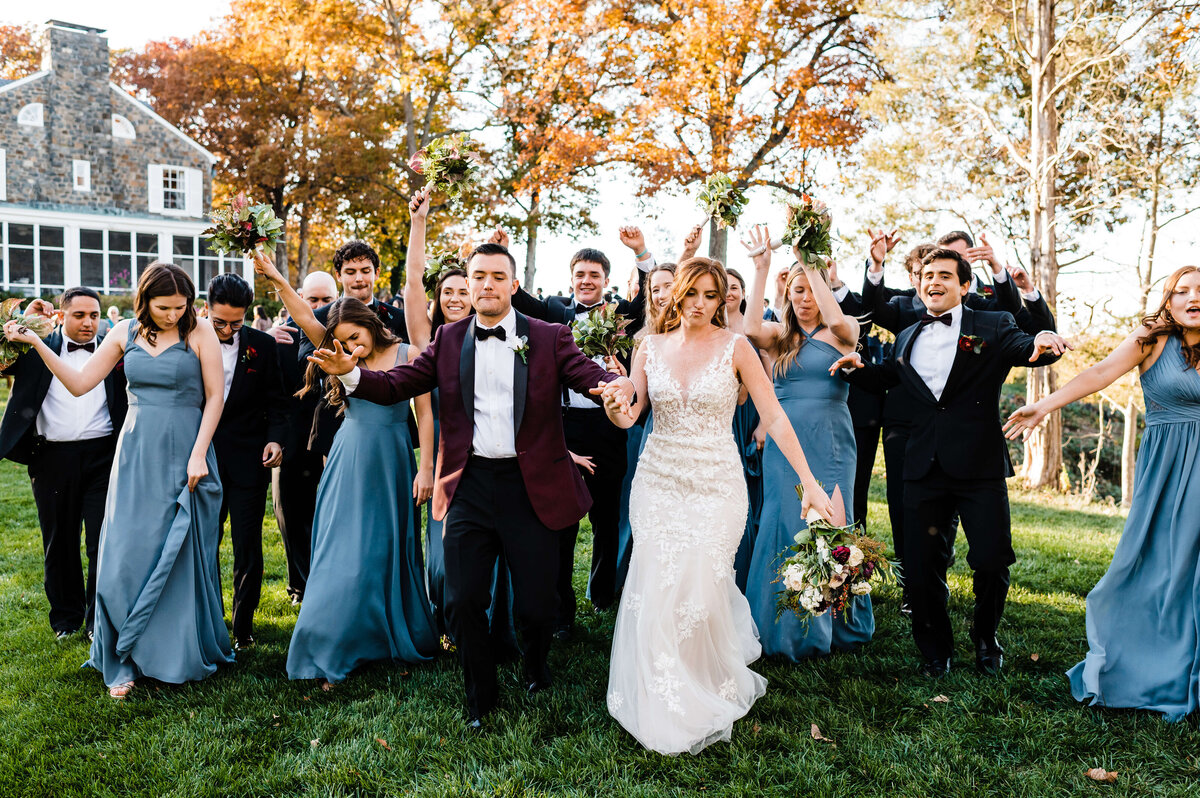 Virginia wedding photographer captures bridal party dancing and walking down a hill at Murray Hill events venue with the bride and groom in the center of the crowd