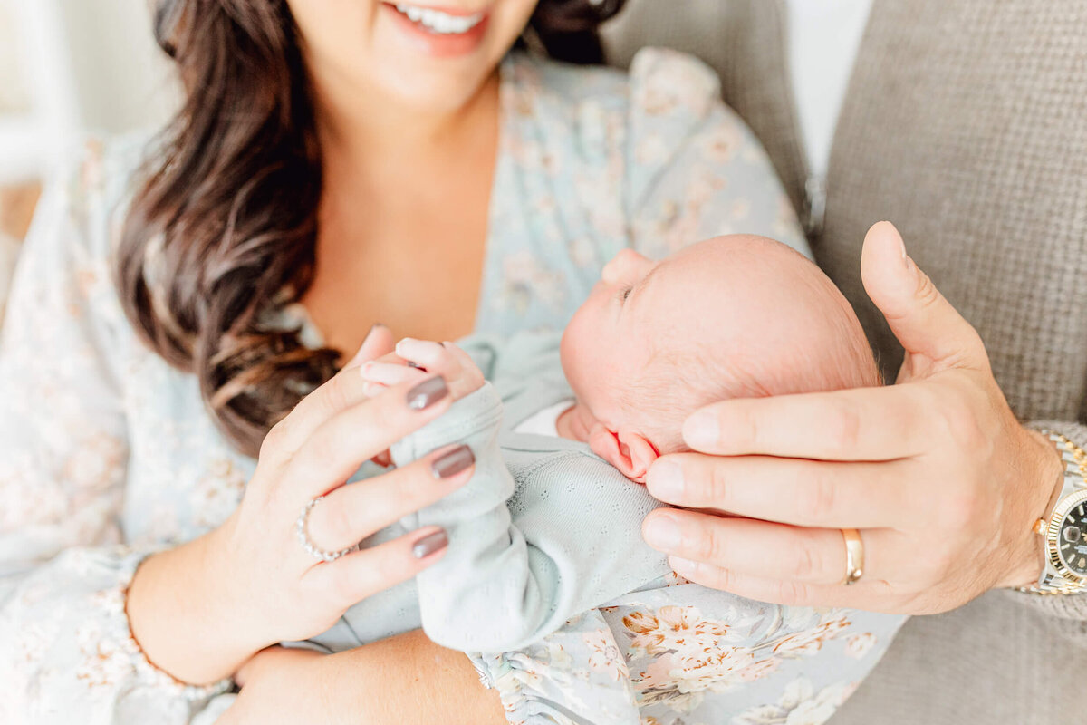 Close up image of newborn grasping mom's fingers while dad's hand cups the baby's head