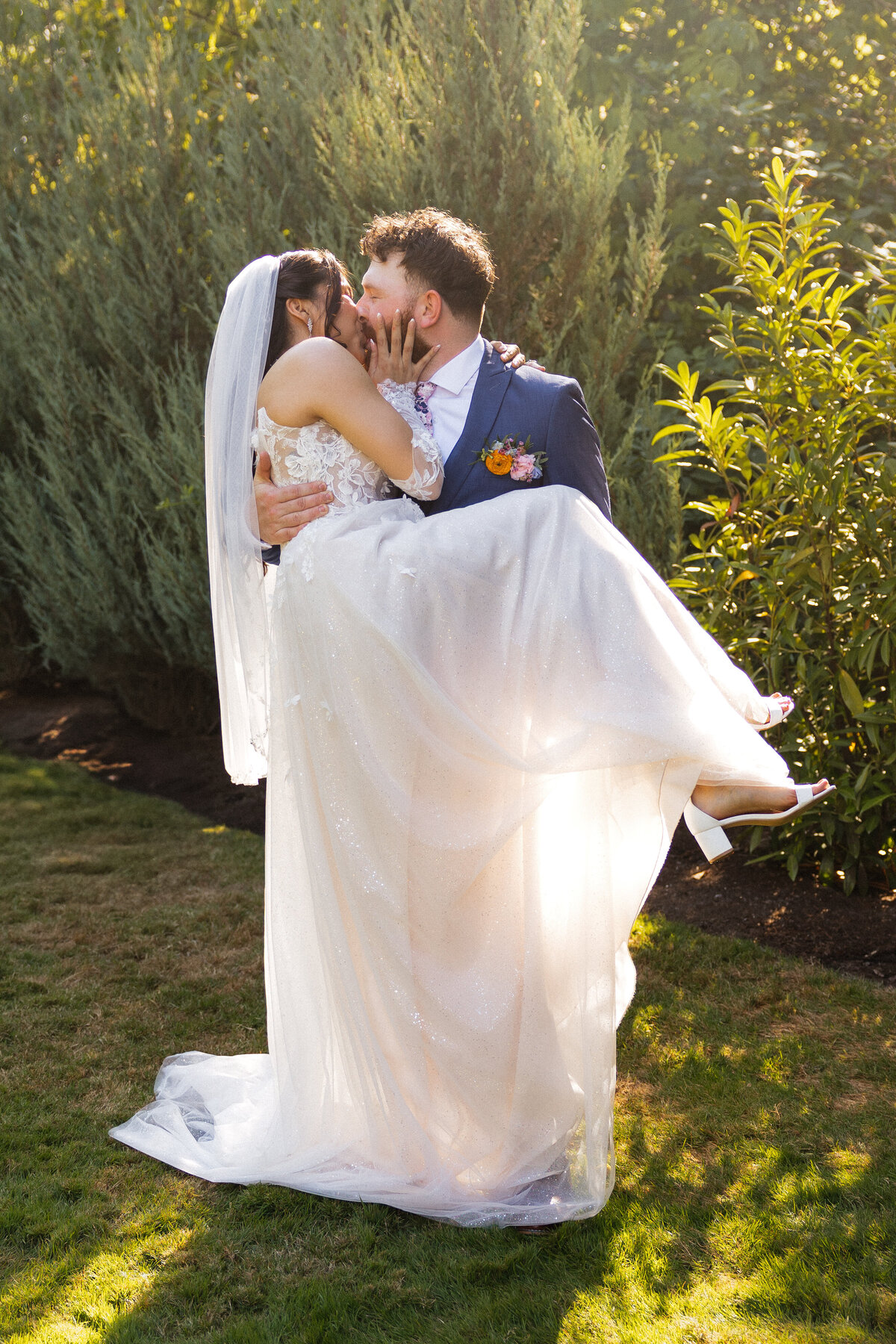 Groom lifts his bride in a romantic moment surrounded by trees.