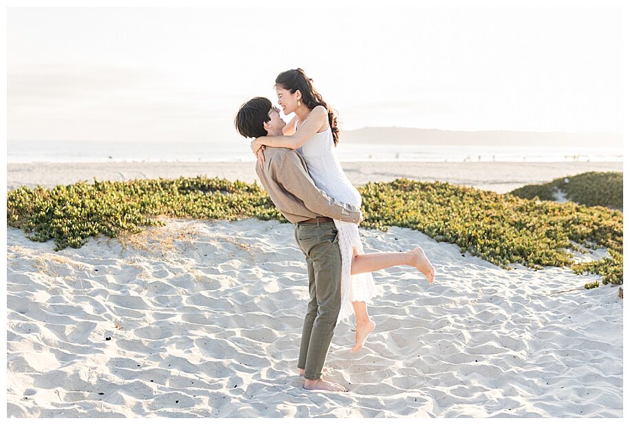 man picking up woman in Coronado Beach sand dunes