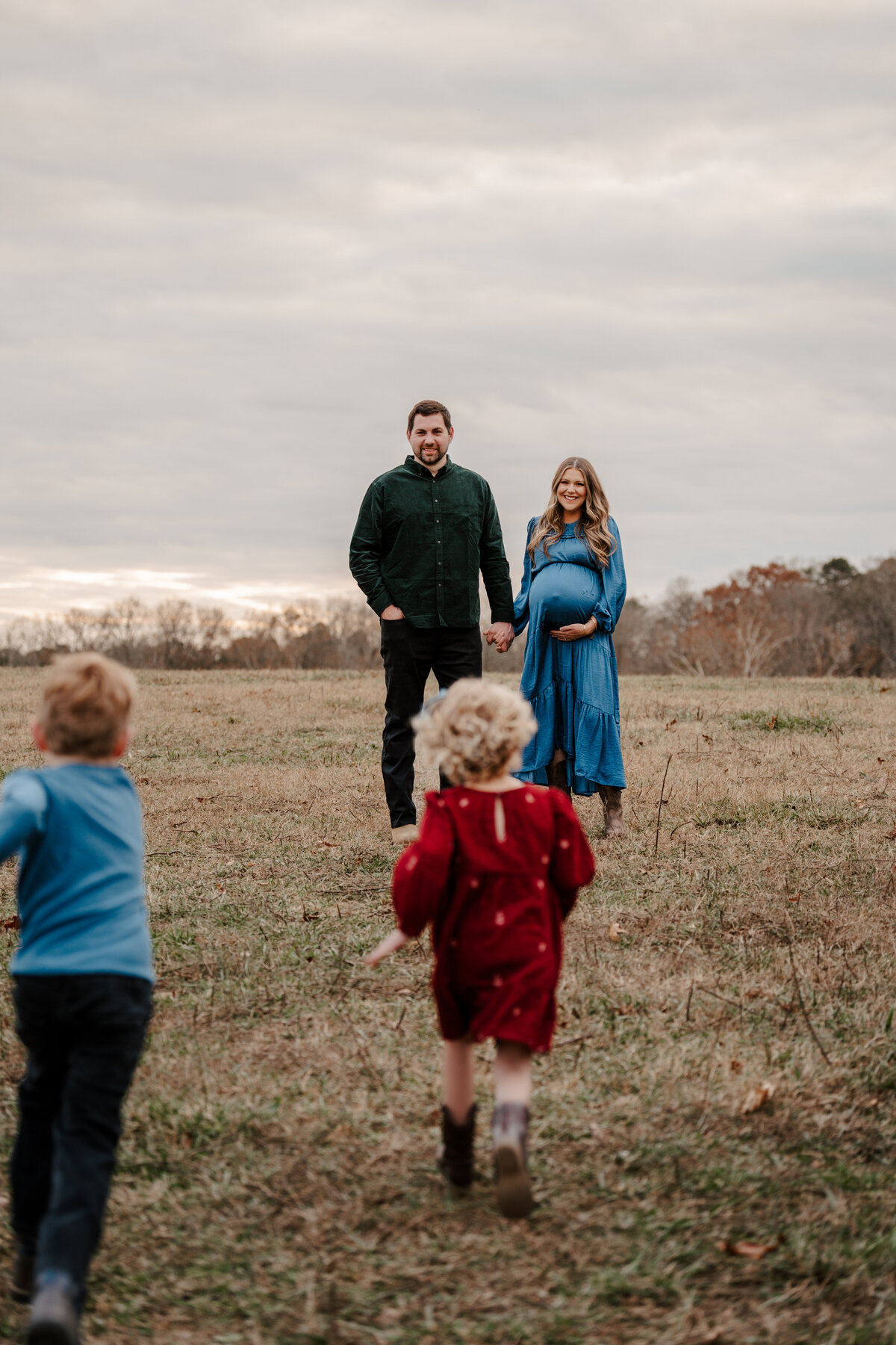 Maternity session—parents-to-be holding hands as their children run toward them in a warm, playful family portrait.