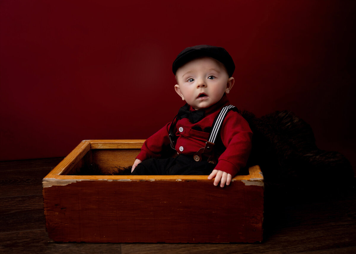Little boy in black hat and suspenders sits in a crate