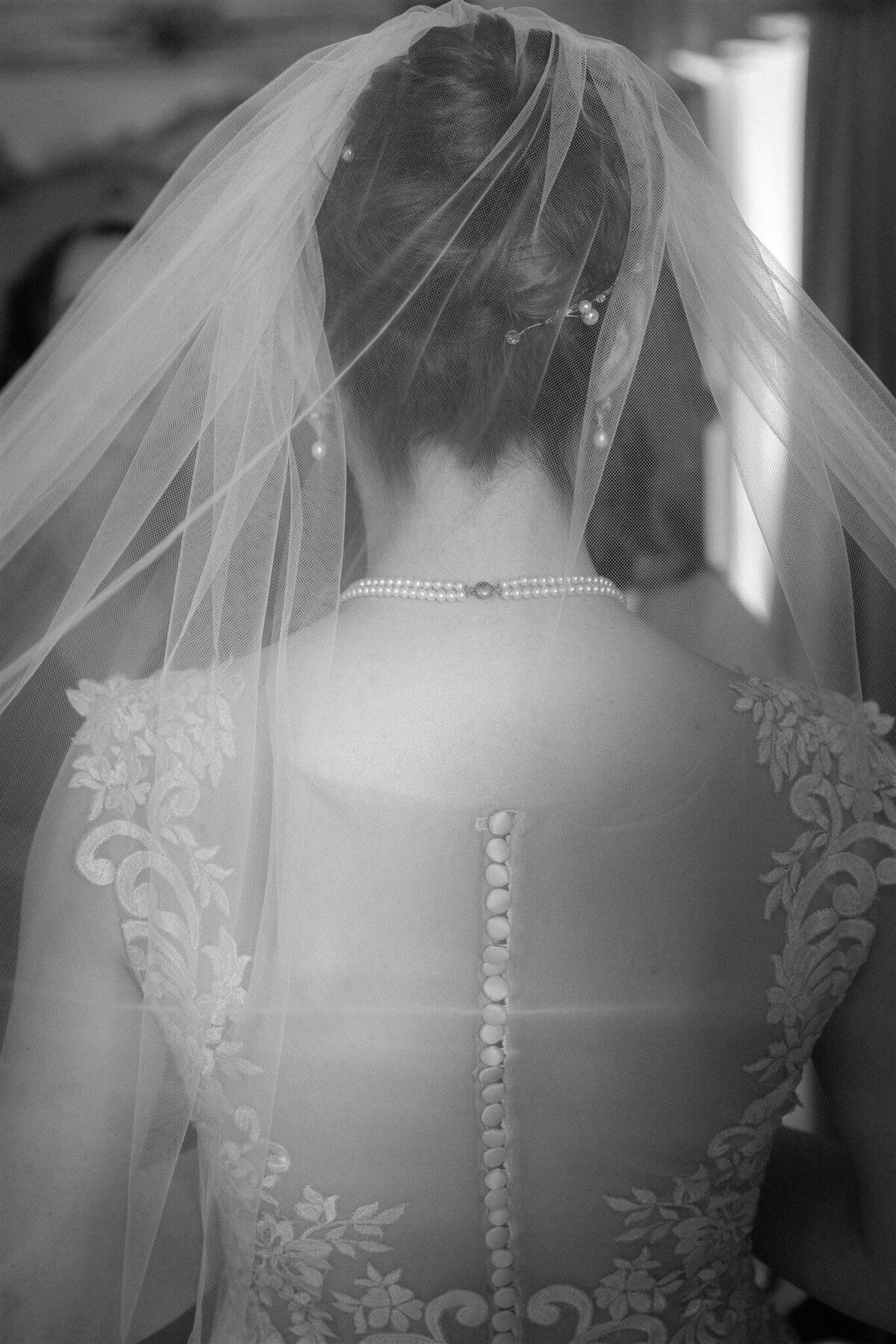 The back of a brides veil and dress as she looks at her reflection.