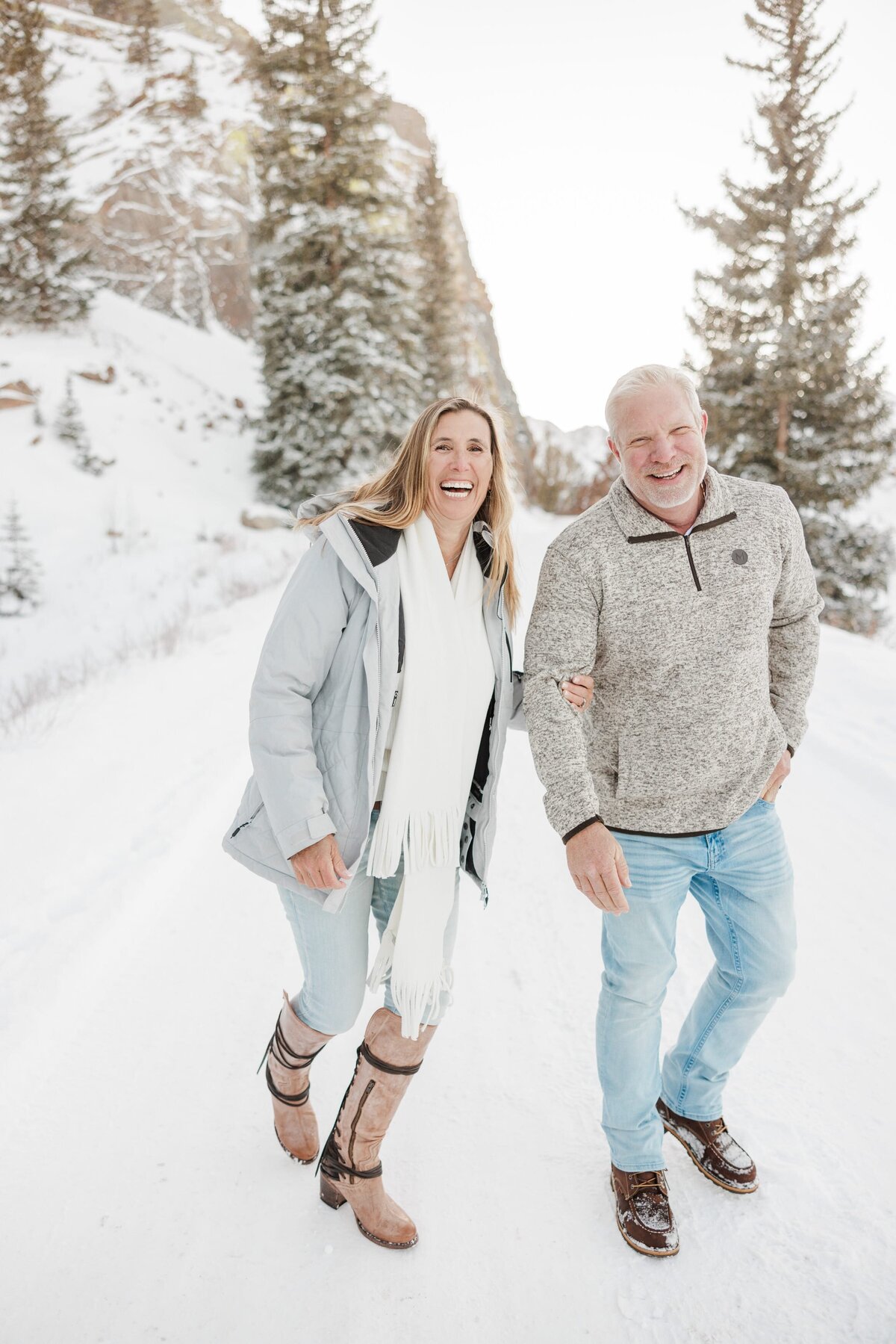 Mom and dad in sweaters and jeans laugh while on a snowy hike