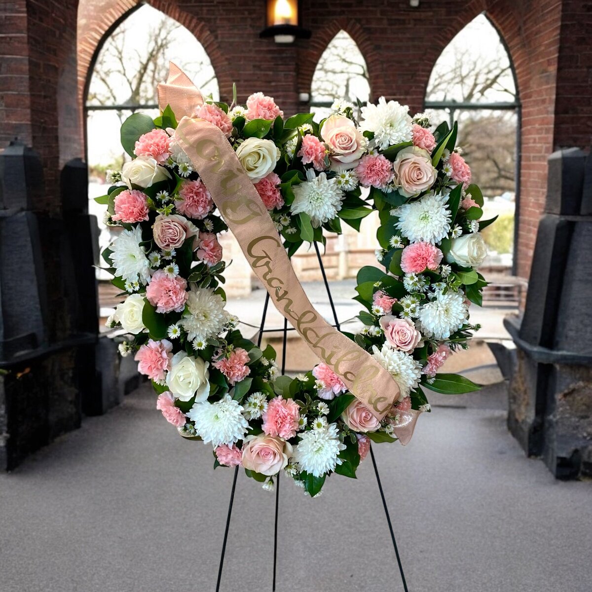 pink and white funeral wreath spray with loving grandchildren on the ribbon