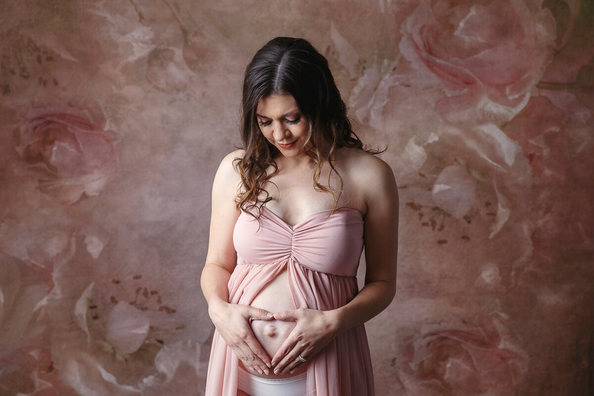 Pregnant woman looking down at her baby belly and shaping her hands into a heart to signify her love for her unborn child