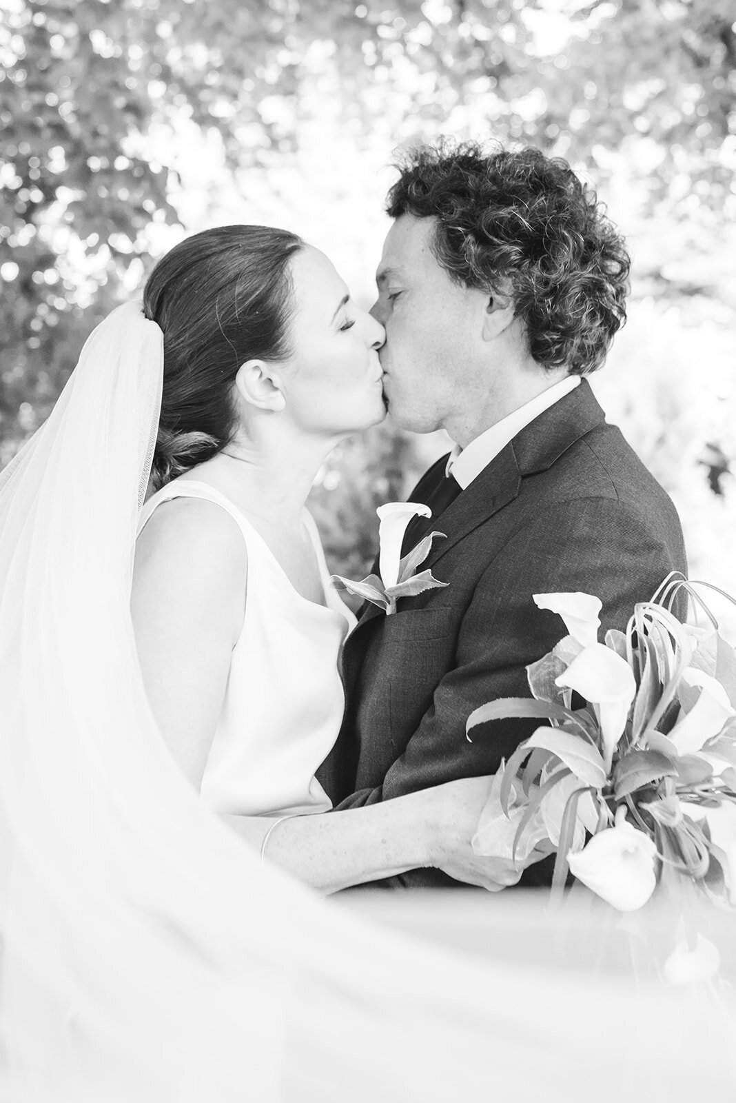 Bride and groom kissing in black and white with the veil sweeping from the left of the image to the right