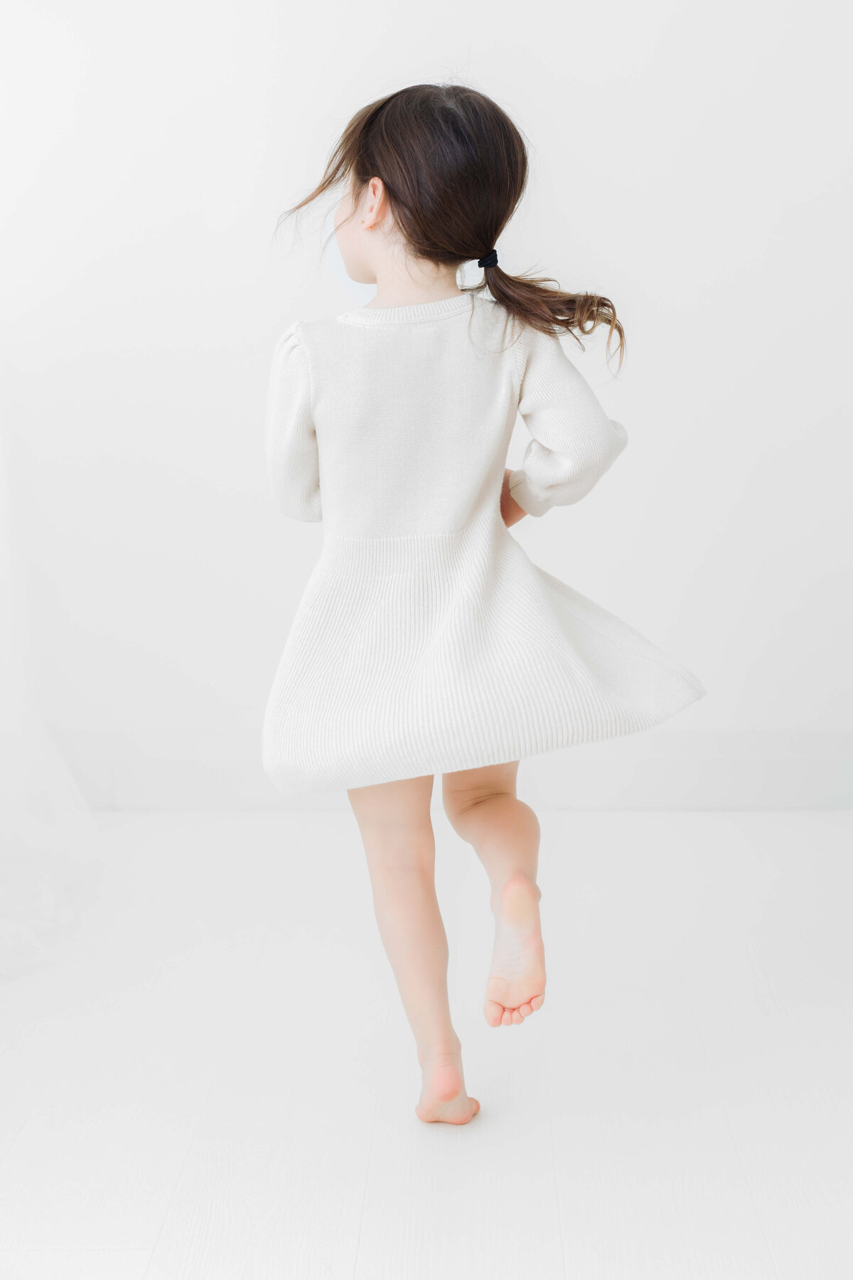 Young girl with brown ponytail and white dress dancing, captured in a studio by Collingwood family photographer Jennifer Walton