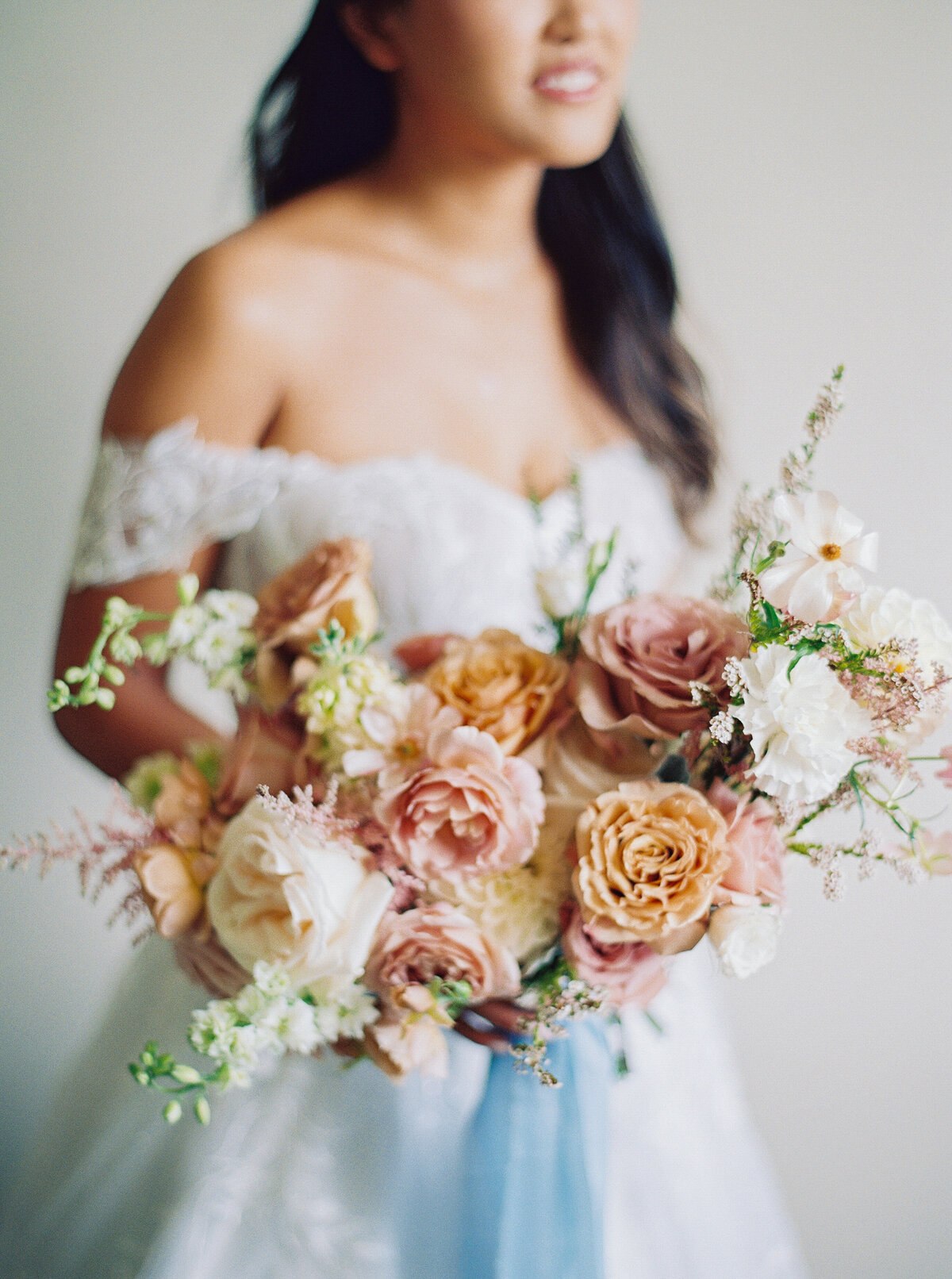 Close-up of romantic bridal bouquet in soft blush and neutral tones with a blue ribbon at Castle Ladyhawke.