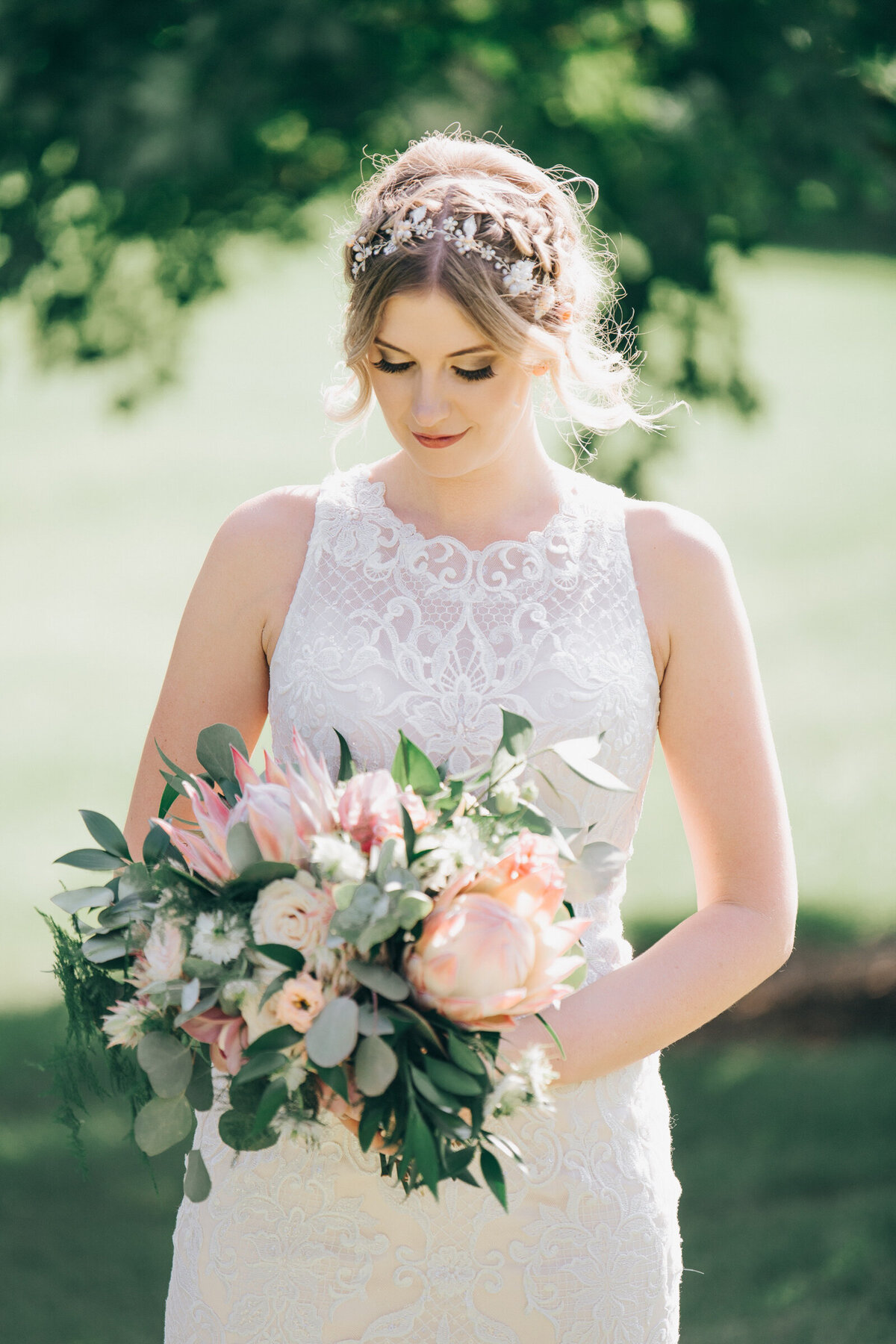 A bride wearing a high neck wedding dress with lace accents looking down at her whimsical blush and green wedding bouquet
