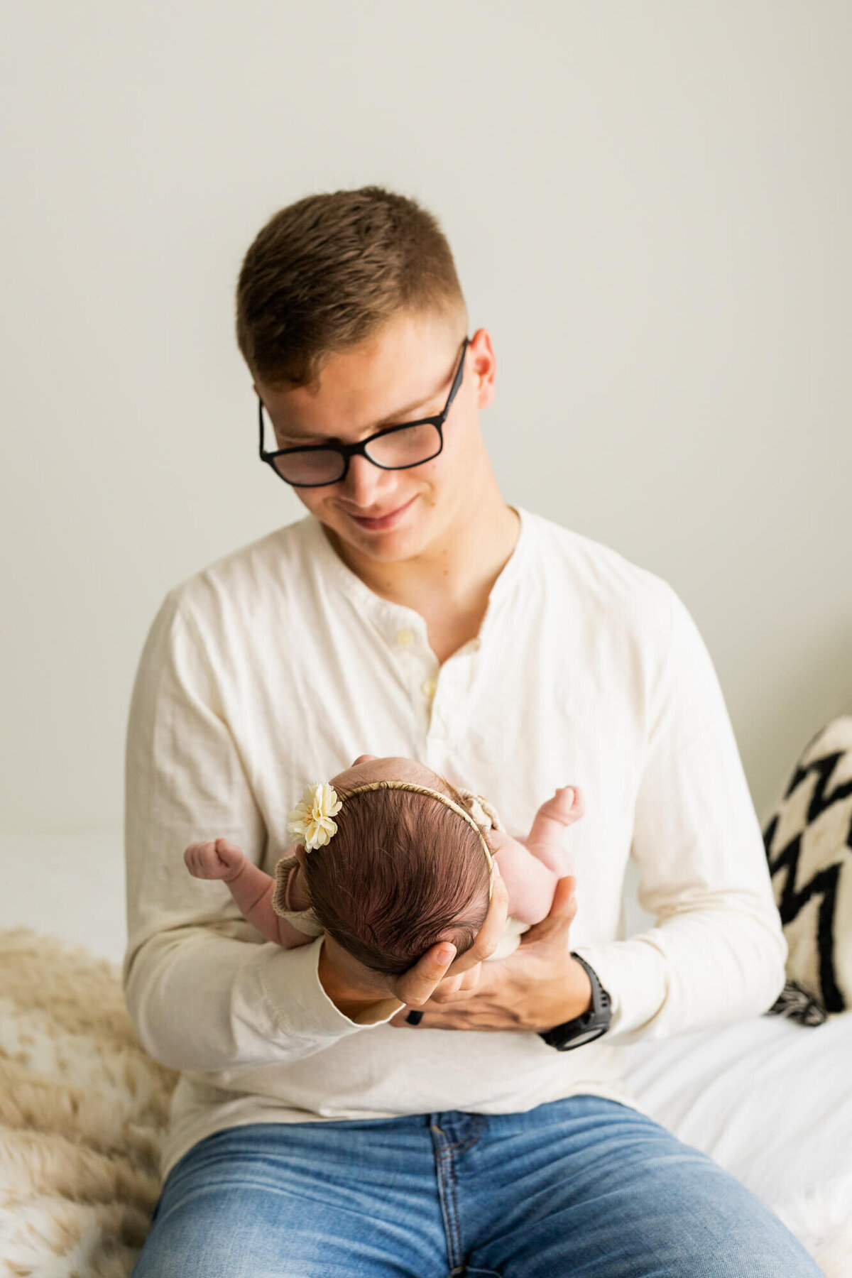 dad in a cream shirt holds his baby girl and smiles at her